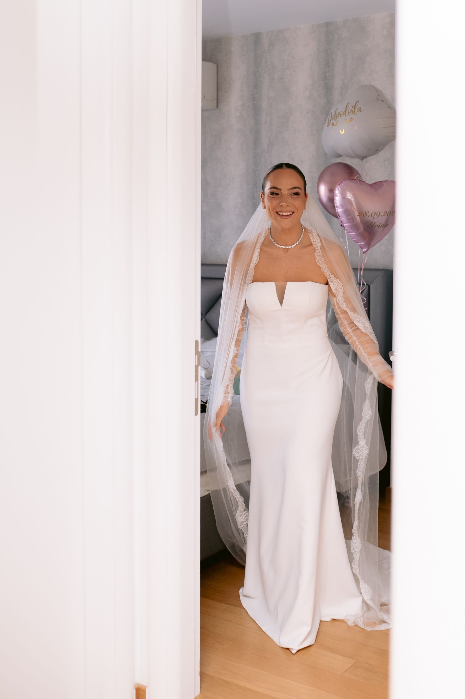 A person wearing a white strapless wedding dress with a flowing veil poses in multiple angles in a bridal fitting room.