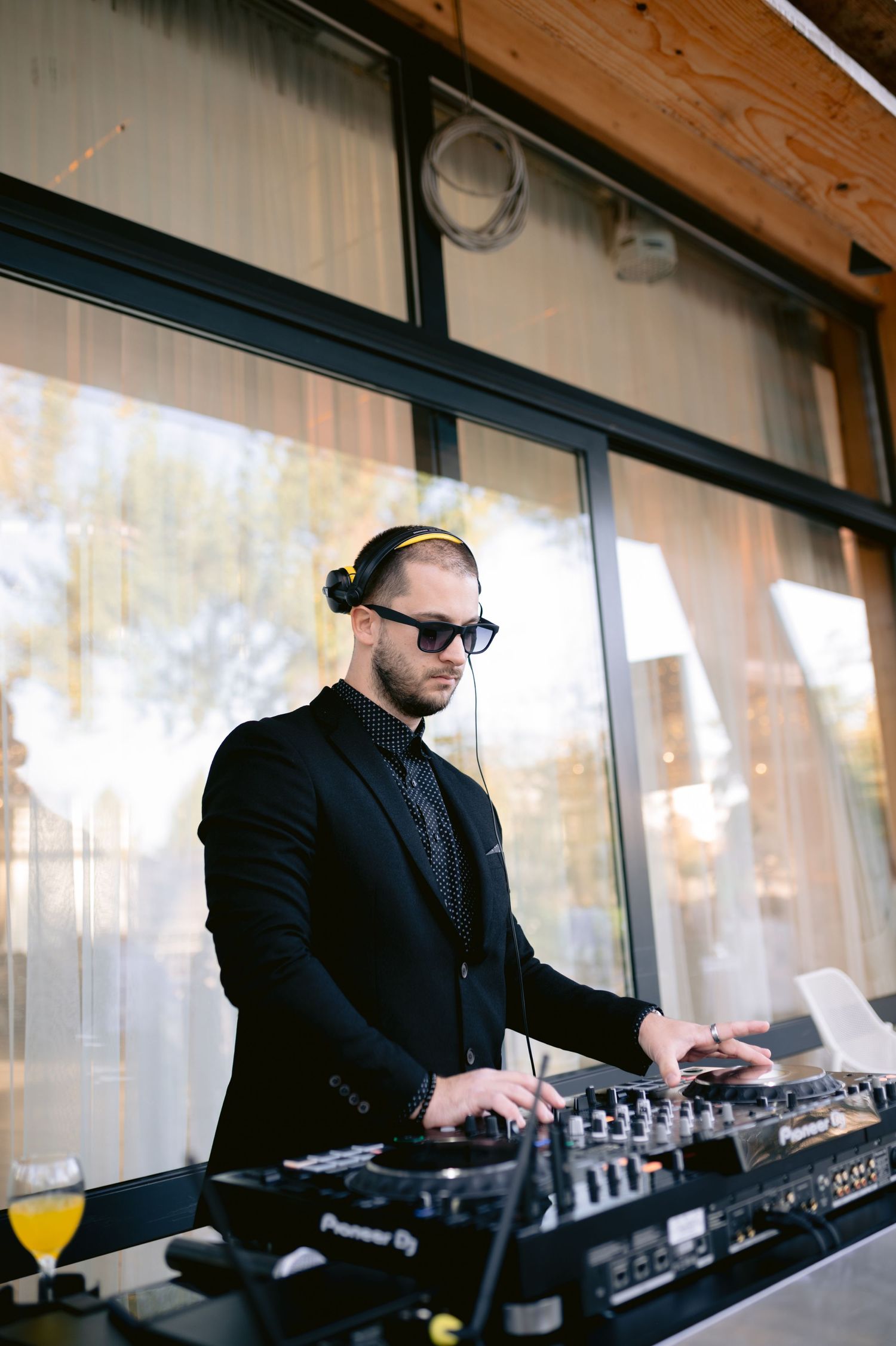 DJ in sunglasses and black suit mixing music at modern venue with professional equipment and mixing deck.