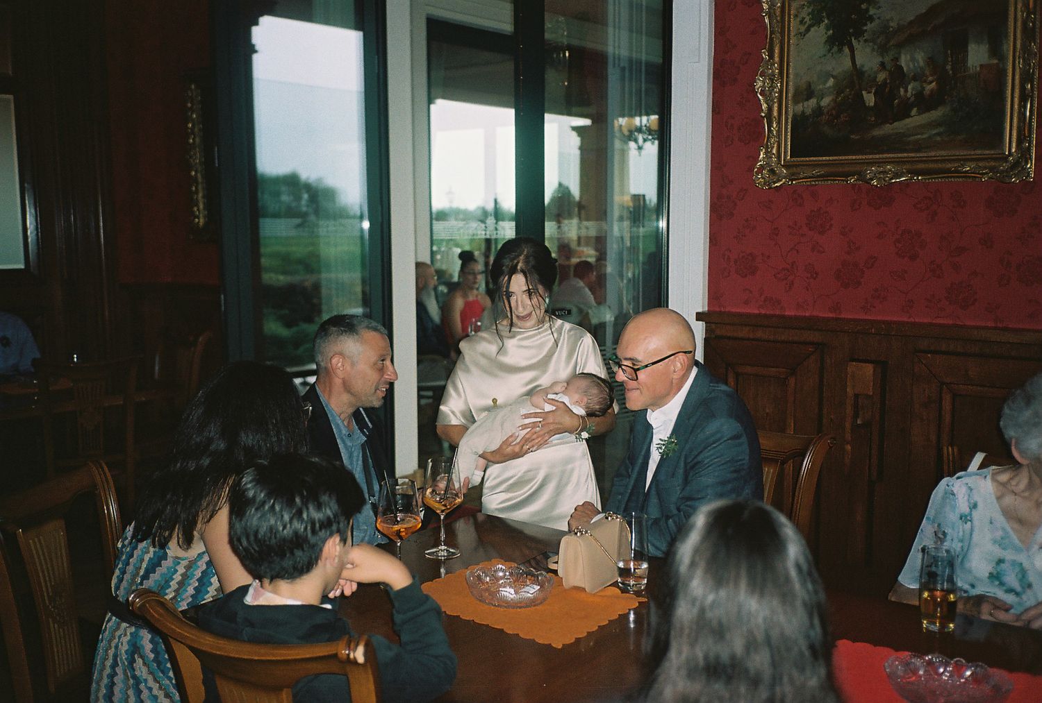 People gathered around tables in a dimly lit restaurant with red walls and classic decor.