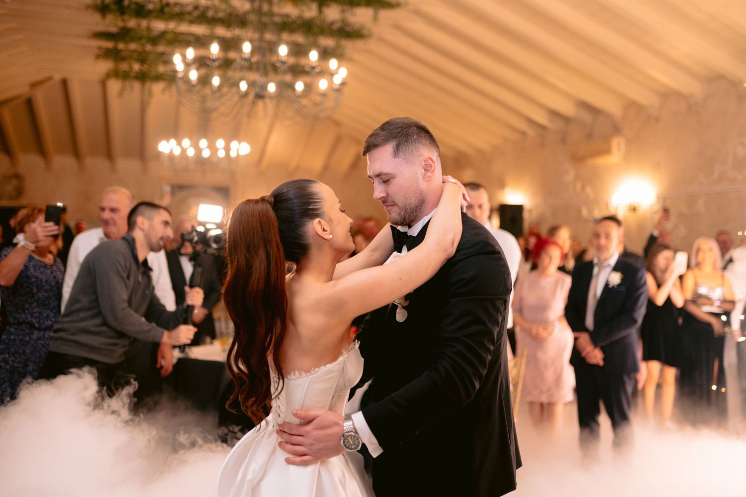 Couples dancing together at an elegant wedding reception under a white tent with chandeliers.