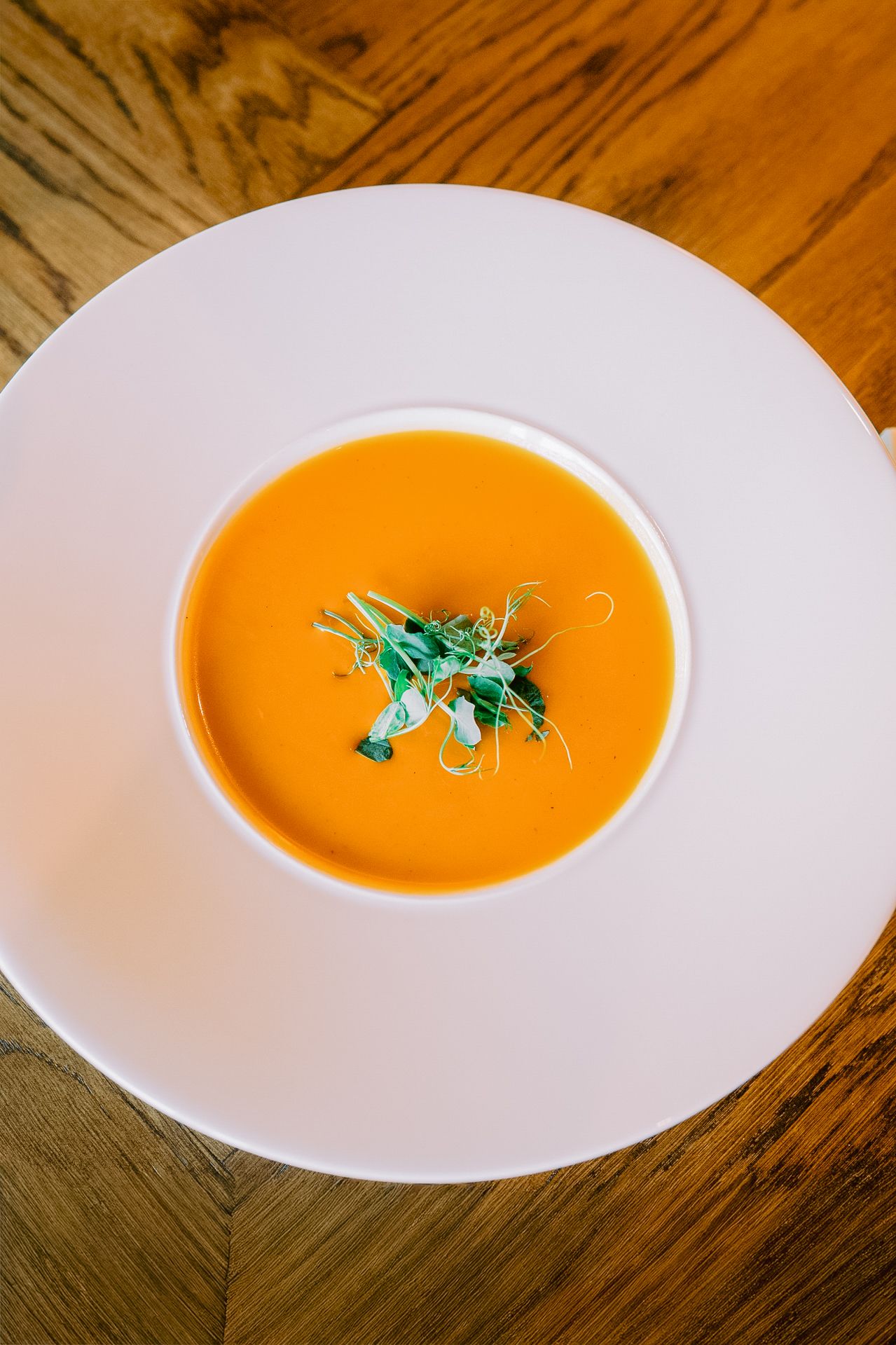 Bright orange creamy soup served in a white bowl with fresh herb garnish.