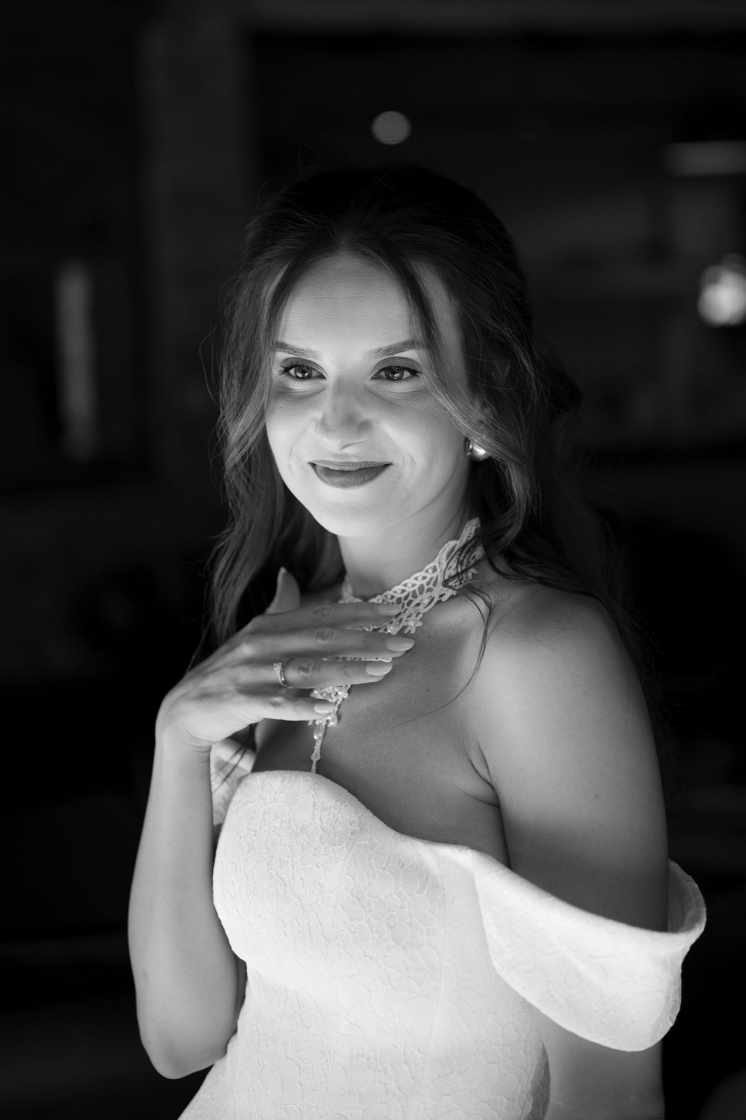 Black and white portrait of an elegant bride wearing a strapless gown, pearl necklace, and earrings, smiling softly.