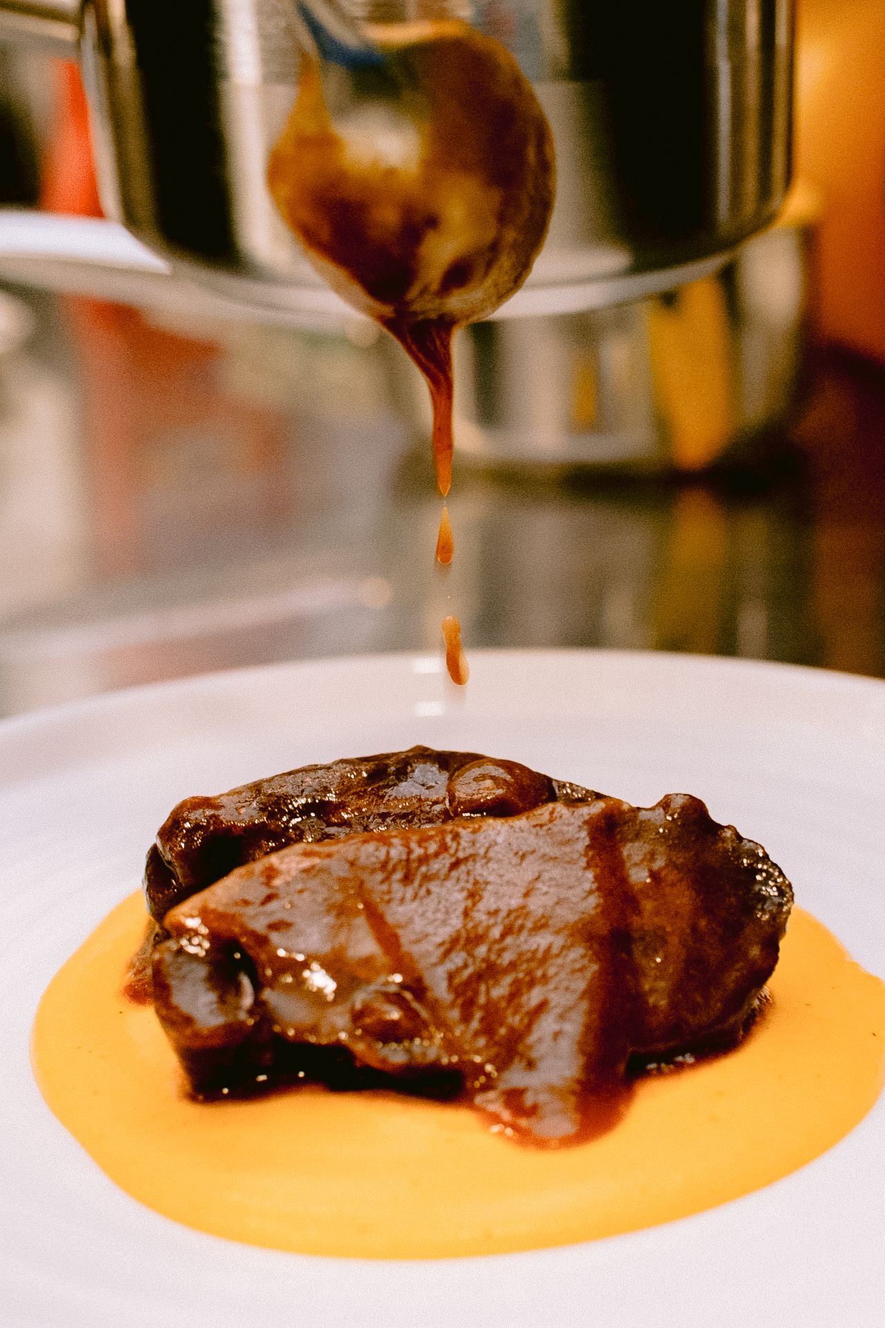 Meat being drizzled with sauce on orange-colored puree base.