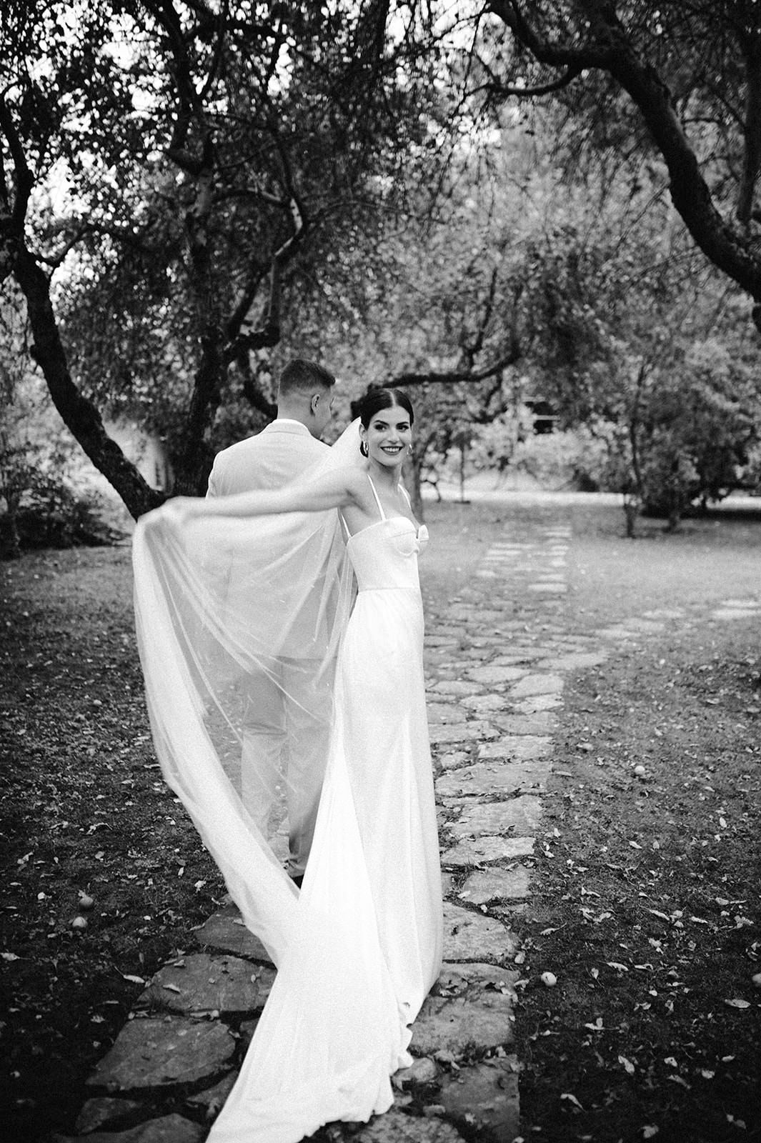 Black and white photo of flowing wedding dress in a garden setting.