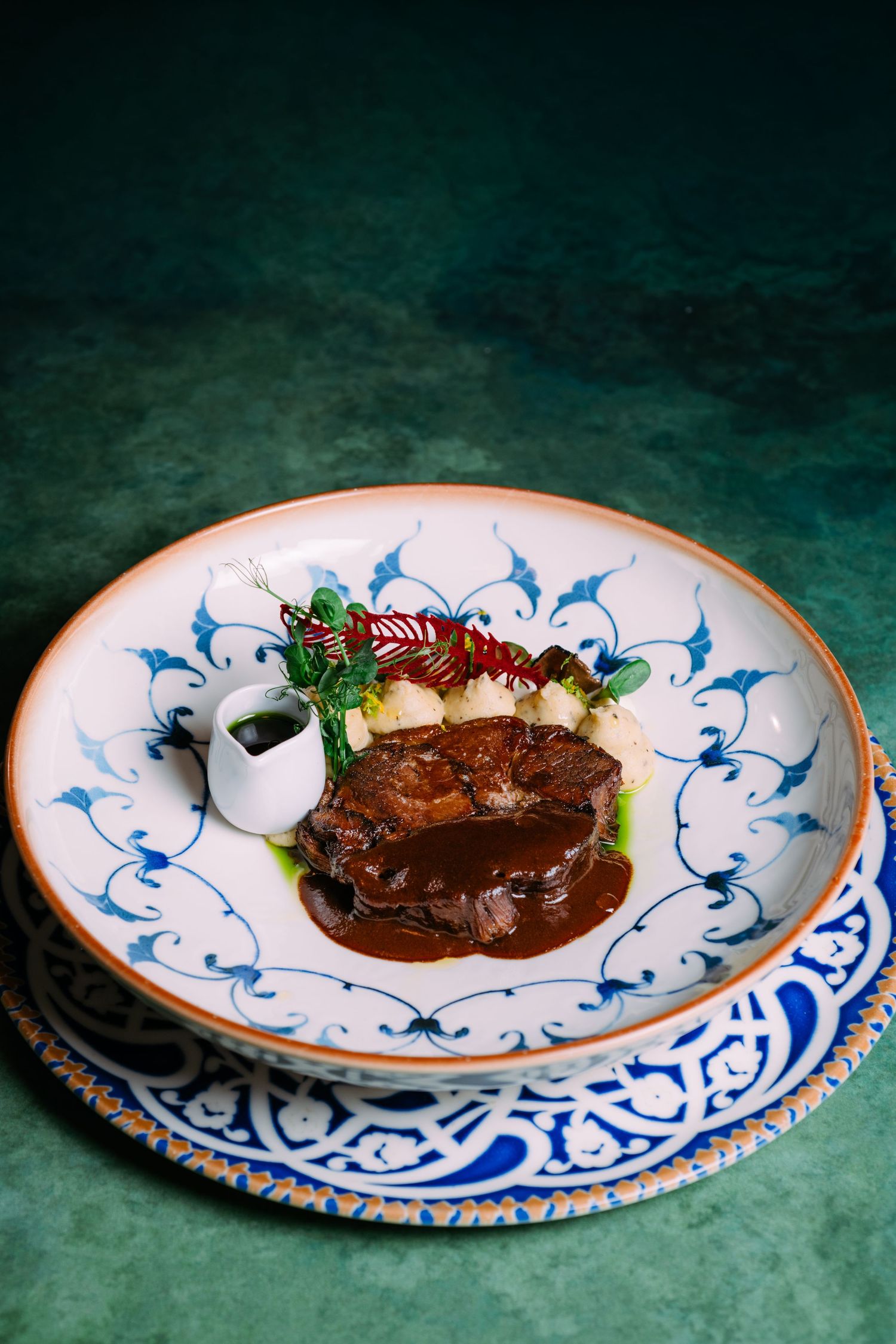 A sequence of plated dishes with rich brown sauces and garnishes on decorative blue and white patterned plates.