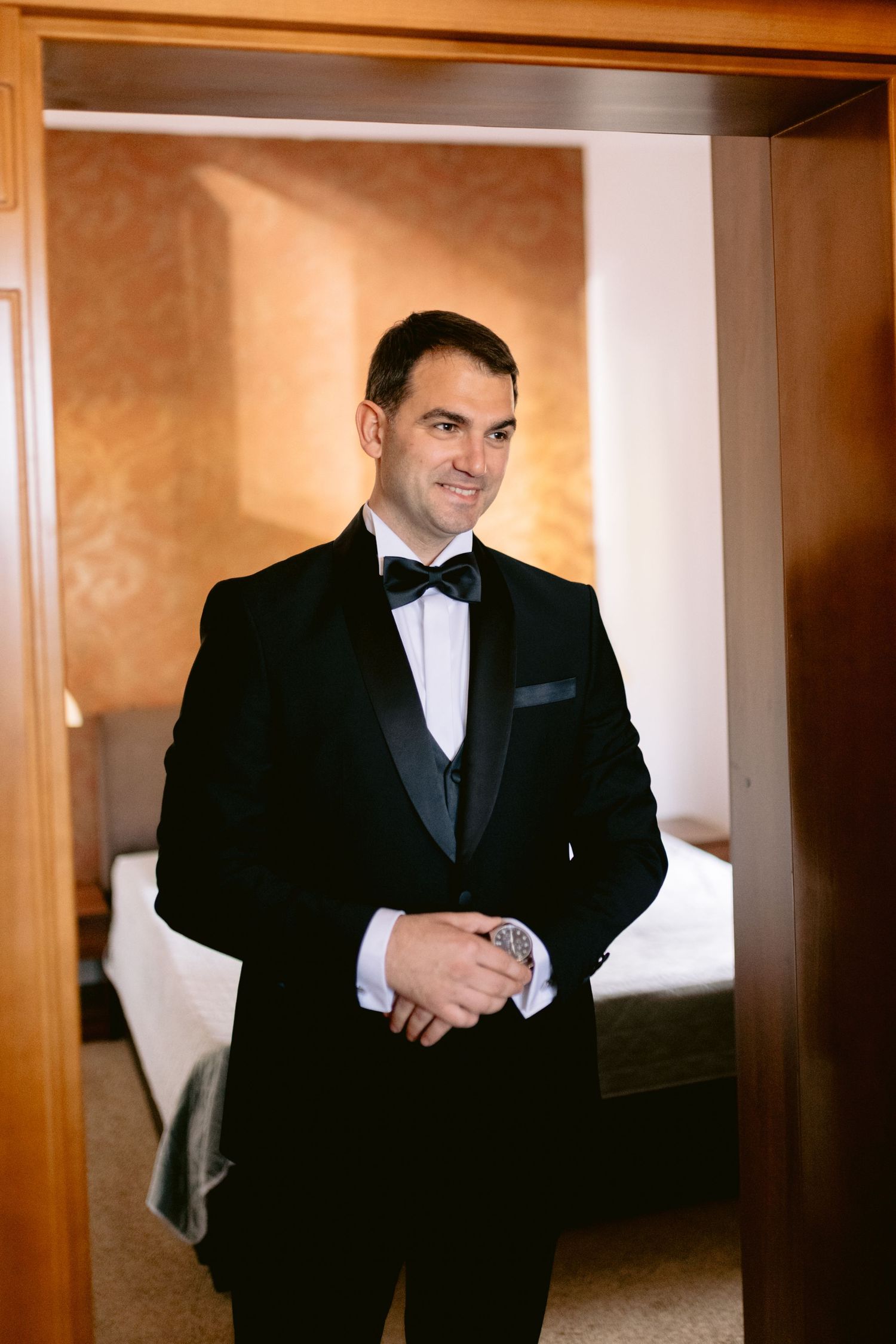 A groom in a classic black tuxedo adjusts his tie while getting ready.