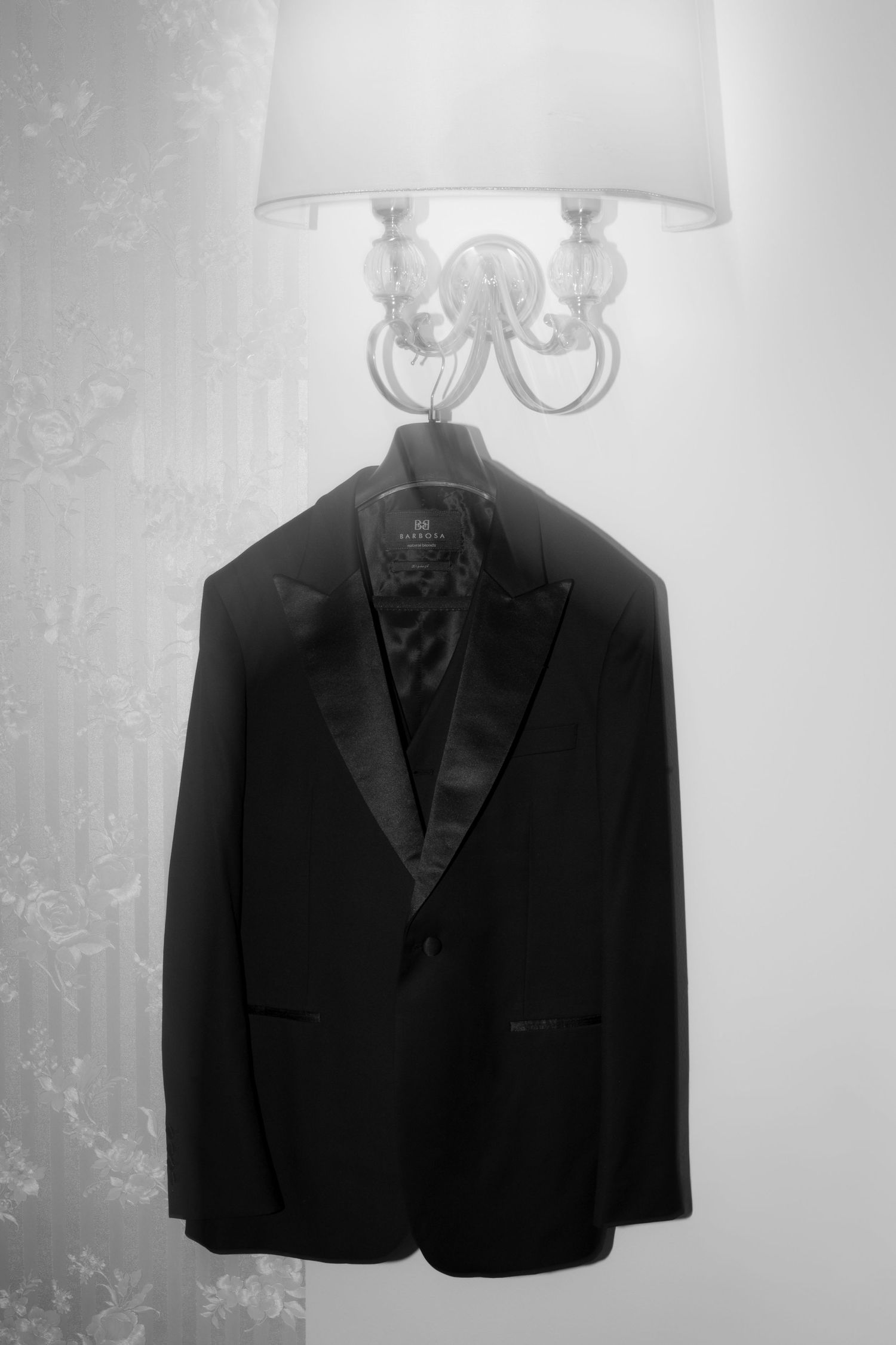 A black suit jacket hangs beneath an elegant white chandelier lamp in a monochromatic composition.