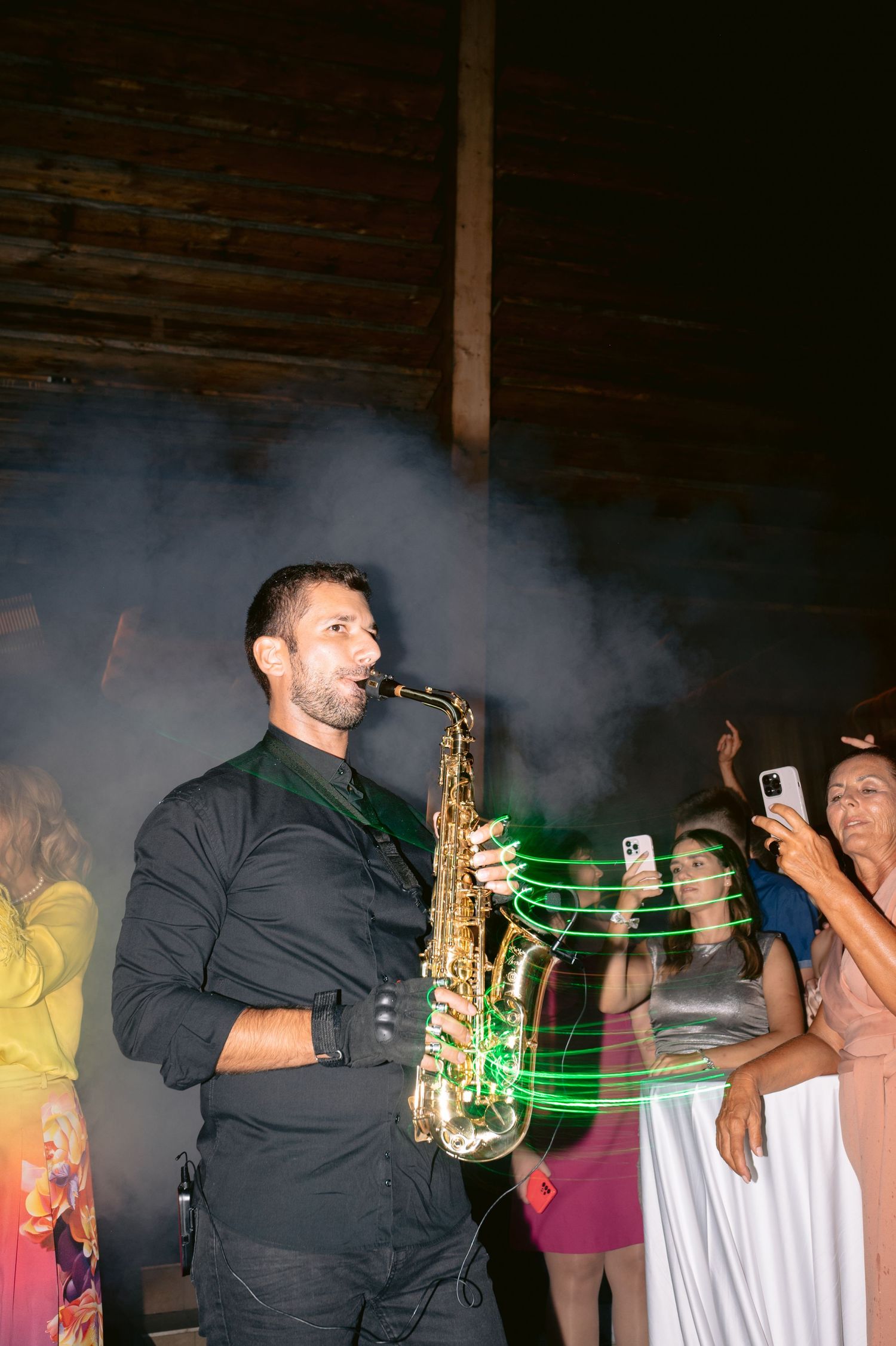 A saxophone player performs on stage amid smoke effects and colorful lighting at a nighttime event.