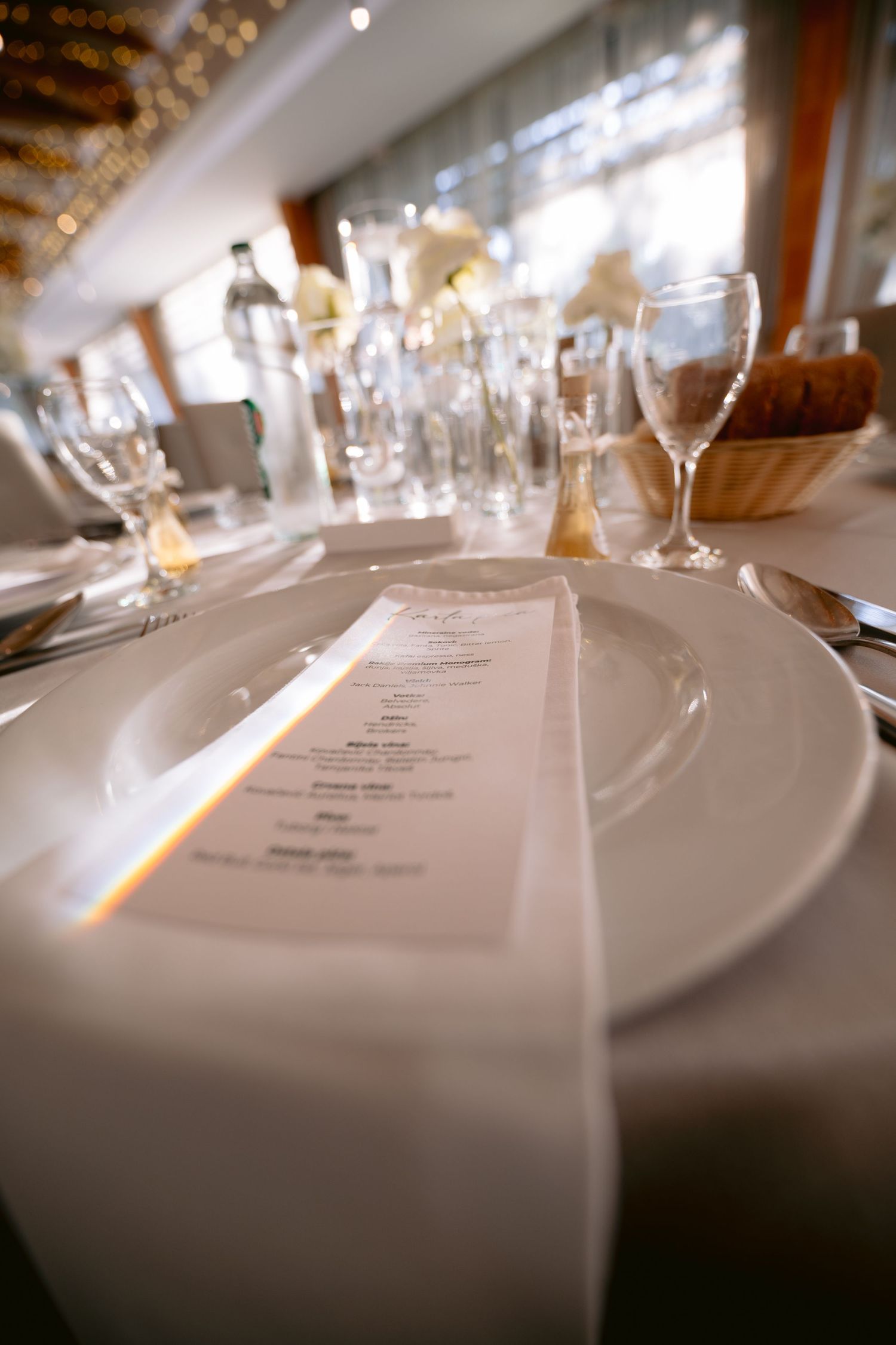 Close-up of wedding reception place setting with menu card on white plate and crystal glassware.