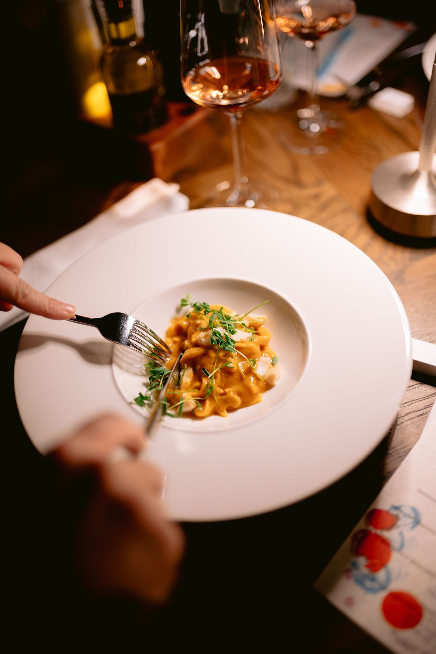 A series of elegant plated pasta dishes being served at a dimly lit restaurant with white tablecloths.