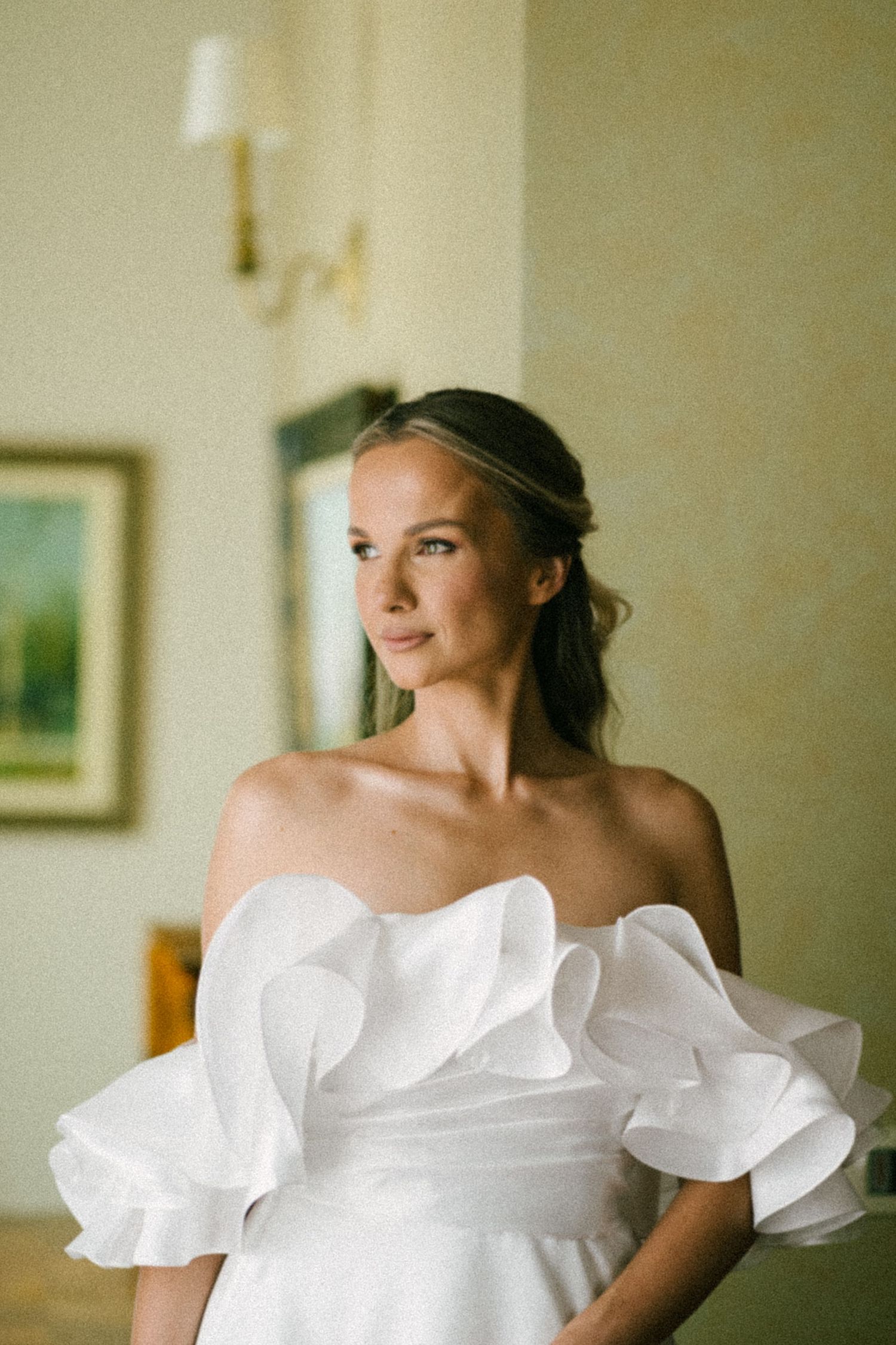Elegant white wedding dress with dramatic ruffled off-shoulder neckline detail in soft natural lighting.