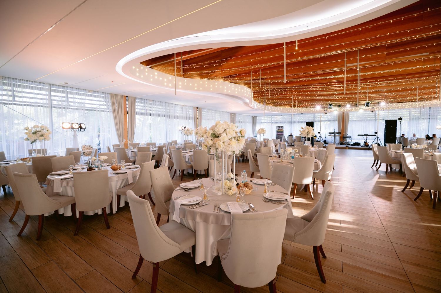 Spacious modern wedding reception venue with white chairs and tables under curved ceiling.