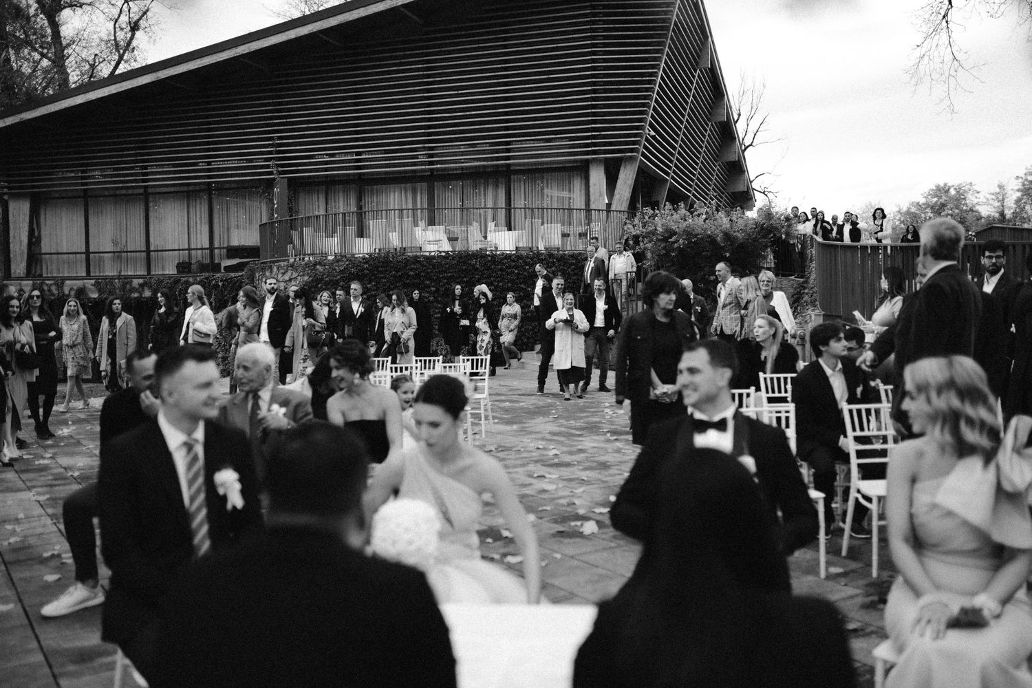 Black and white photo of a wedding ceremony with bride and groom seated outdoors near a barn.