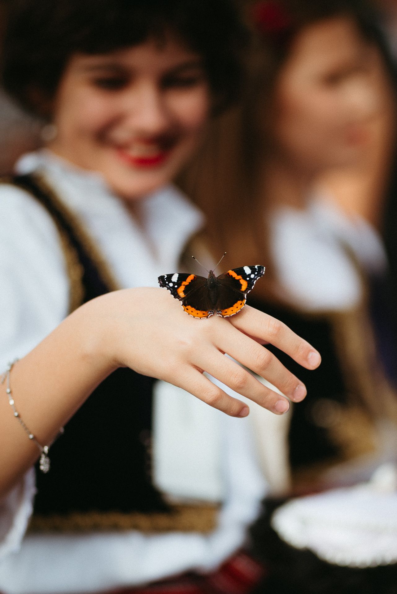 Smiling girl in traditional costume with a Red Admiral butterfly resting on her outstretched hand.