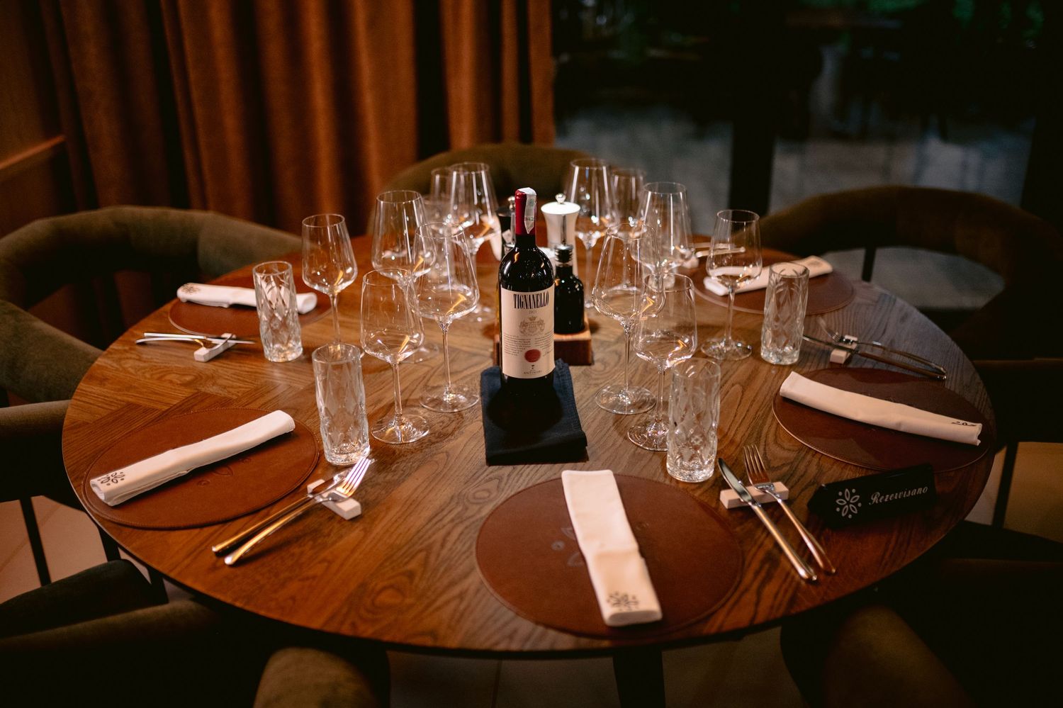 Elegant round dining tables set with crystal glasses and white napkins in a dimly lit upscale restaurant interior.