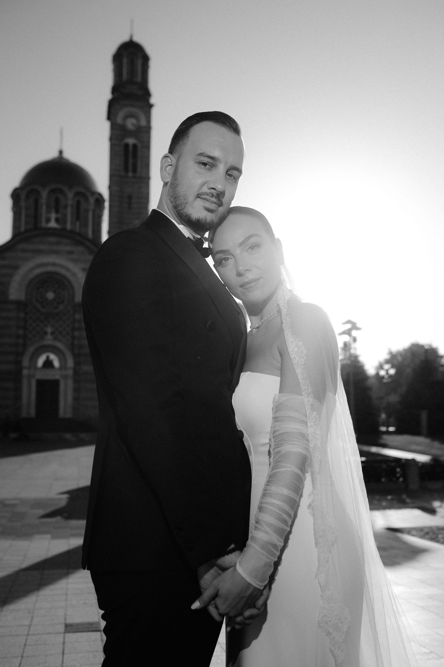 A romantic black and white wedding photo series showing a couple in formal attire posing near a church exterior.