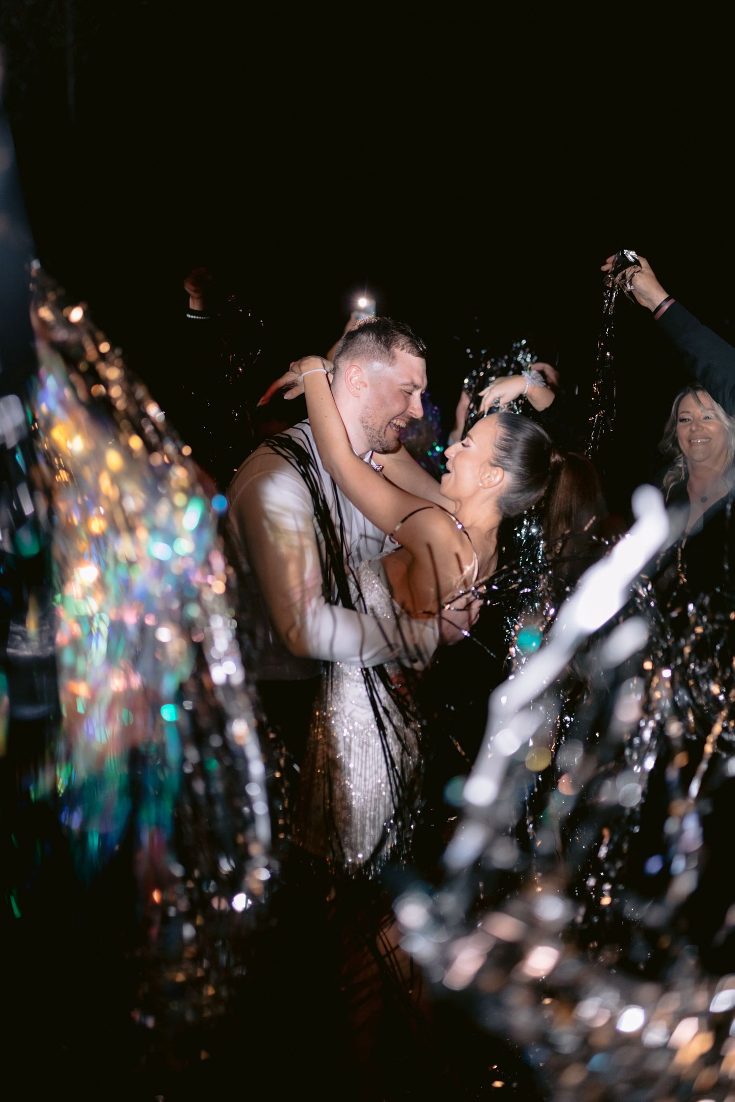 A romantic couple embraces during their first dance at a wedding reception with sparkling lights in the background.