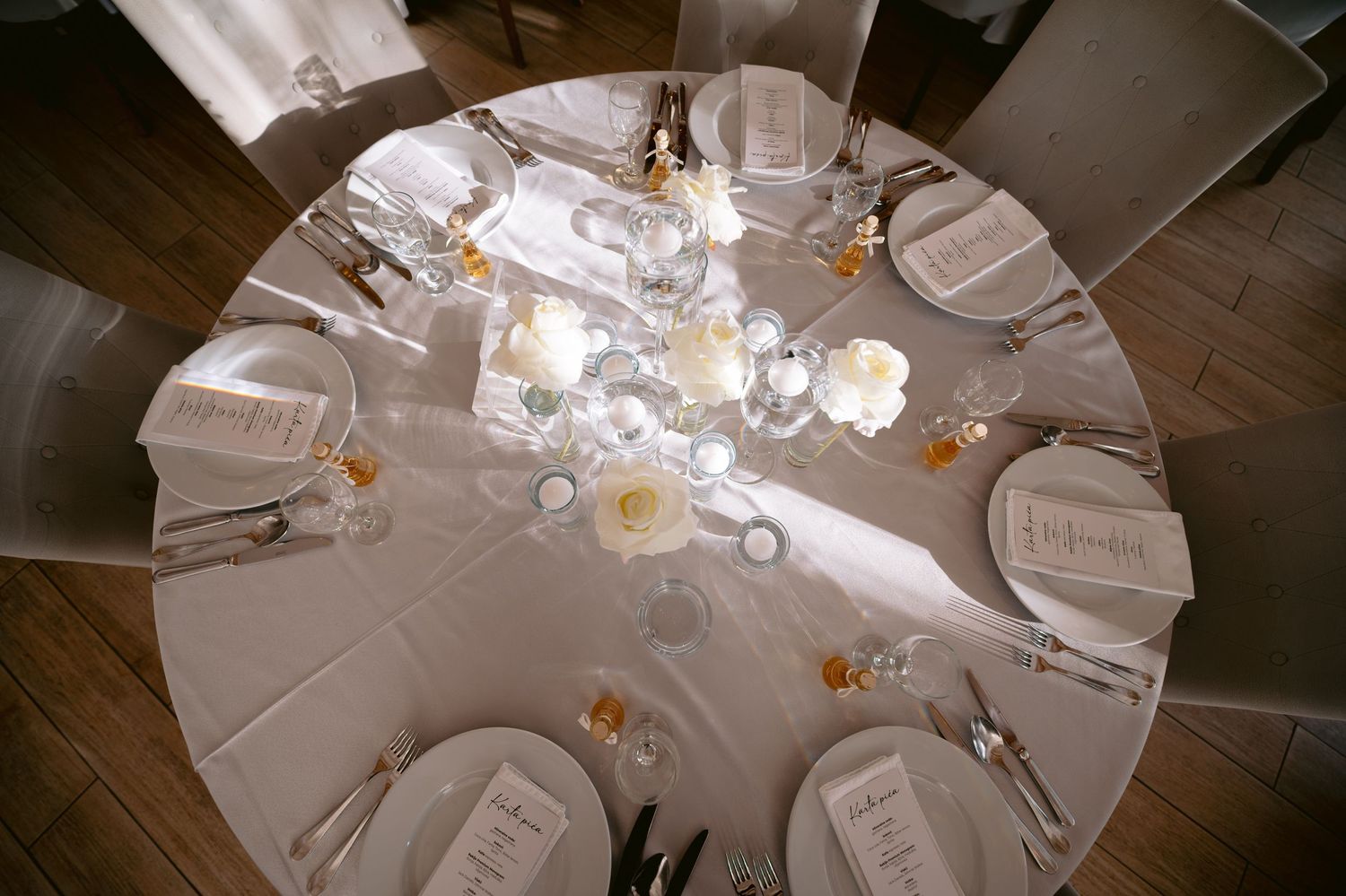 Elegant round dining table set with white place settings, floral centerpieces, and glowing candlelight for a formal event.