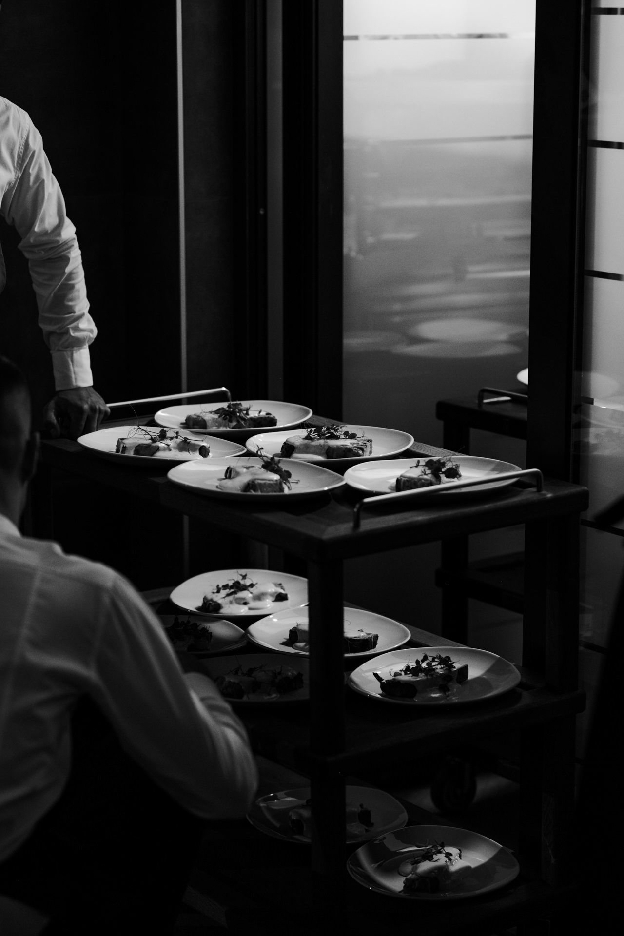 Multiple white plates with food being served in a dimly lit restaurant setting.