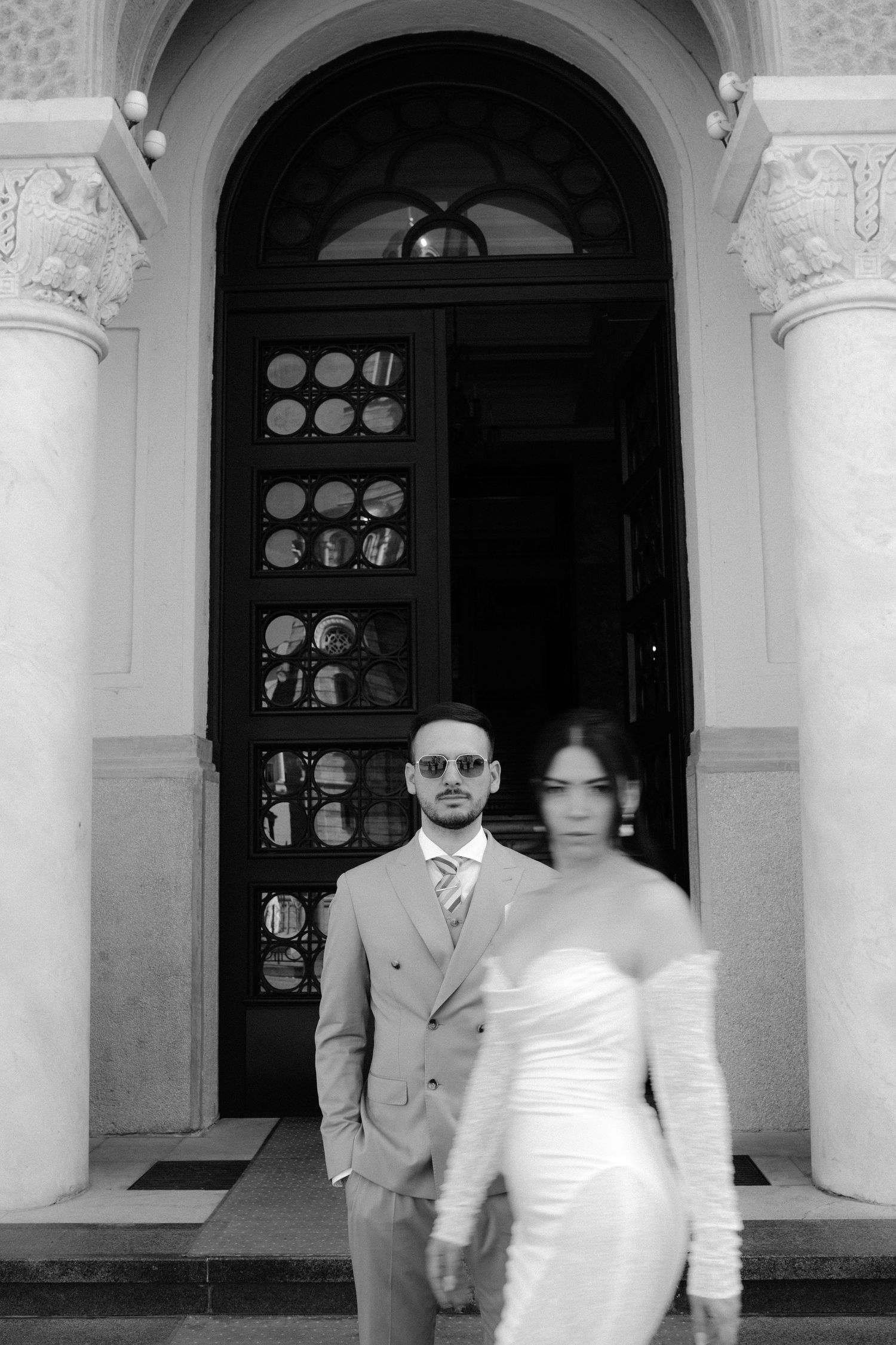 Crno-bijela fotografija mladoženje koji stoji i mlade koja hoda ispred njega kod Bankog dvora u Banja Luci.
