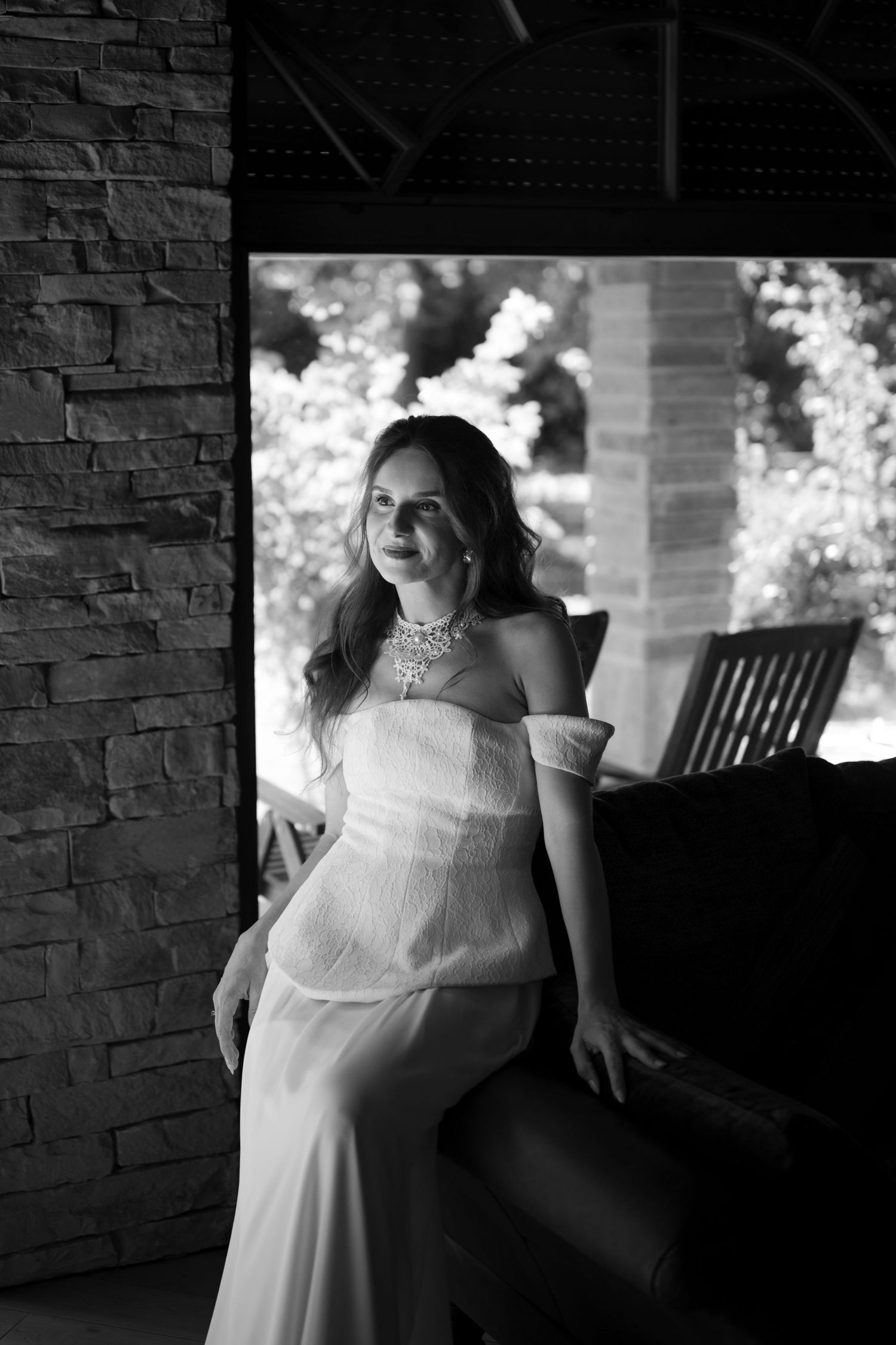 Crno-bijeli portret elegantne mlade u vjenElegant bride in white off-shoulder gown with diamond necklace seated in black and white portrait.
