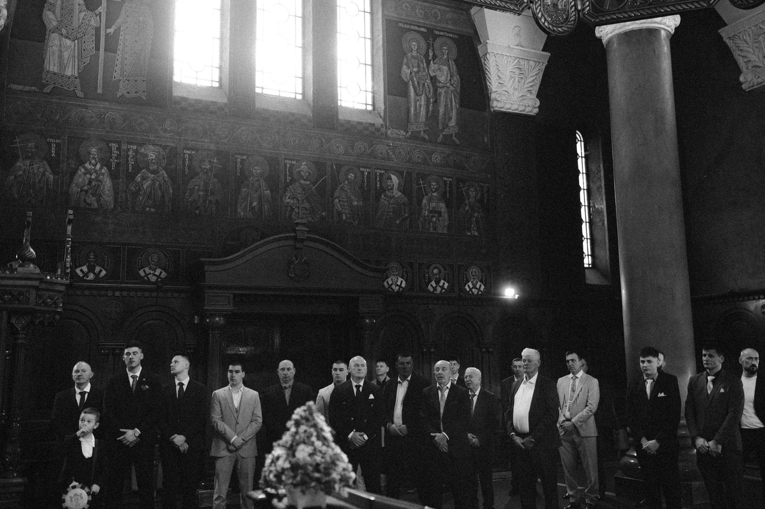 Black and white photo of men standing in a church interior with Byzantine mosaics and floral arrangement.