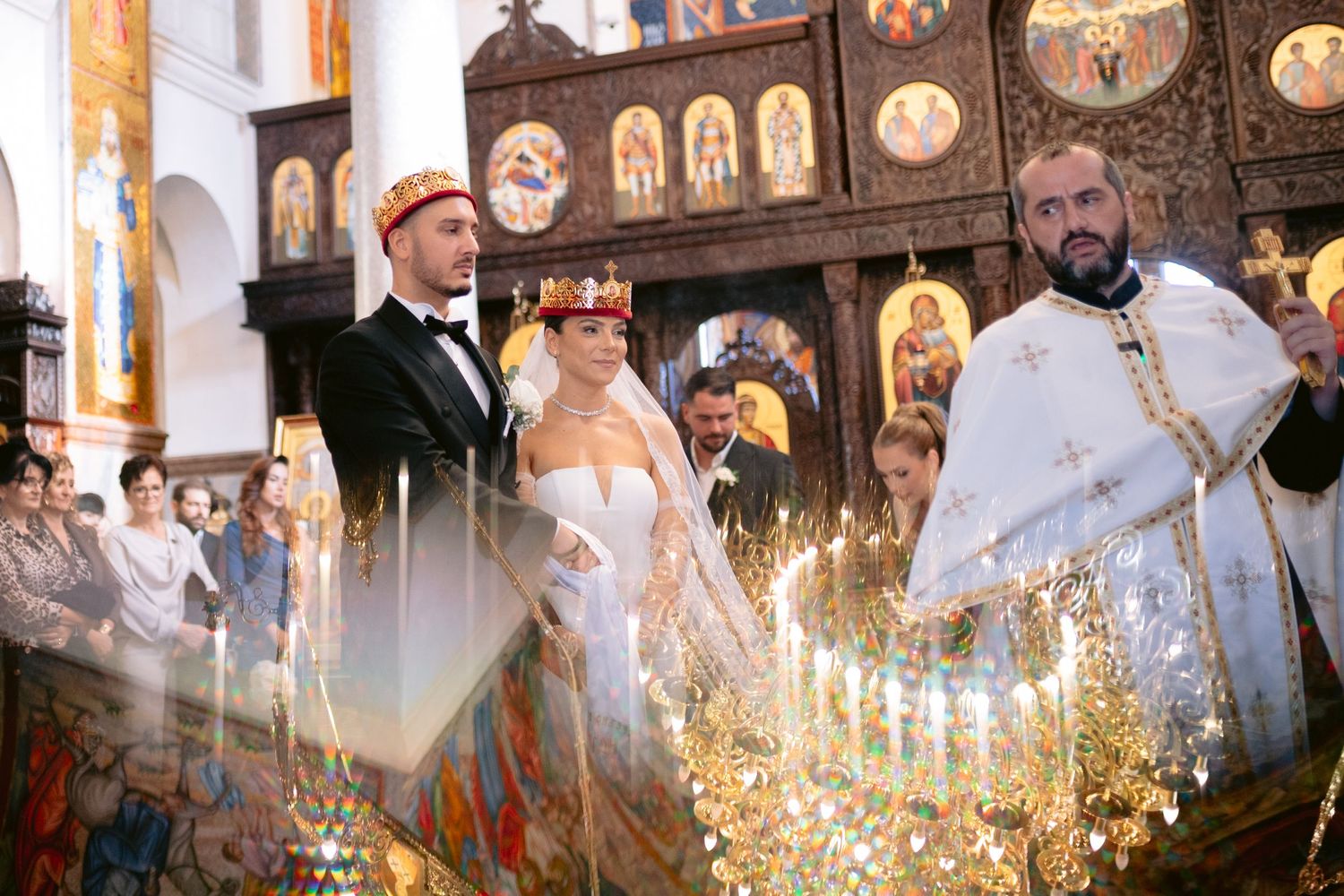 Orthodox priests in white robes conduct a religious ceremony with candles and incense in an ornate church setting.