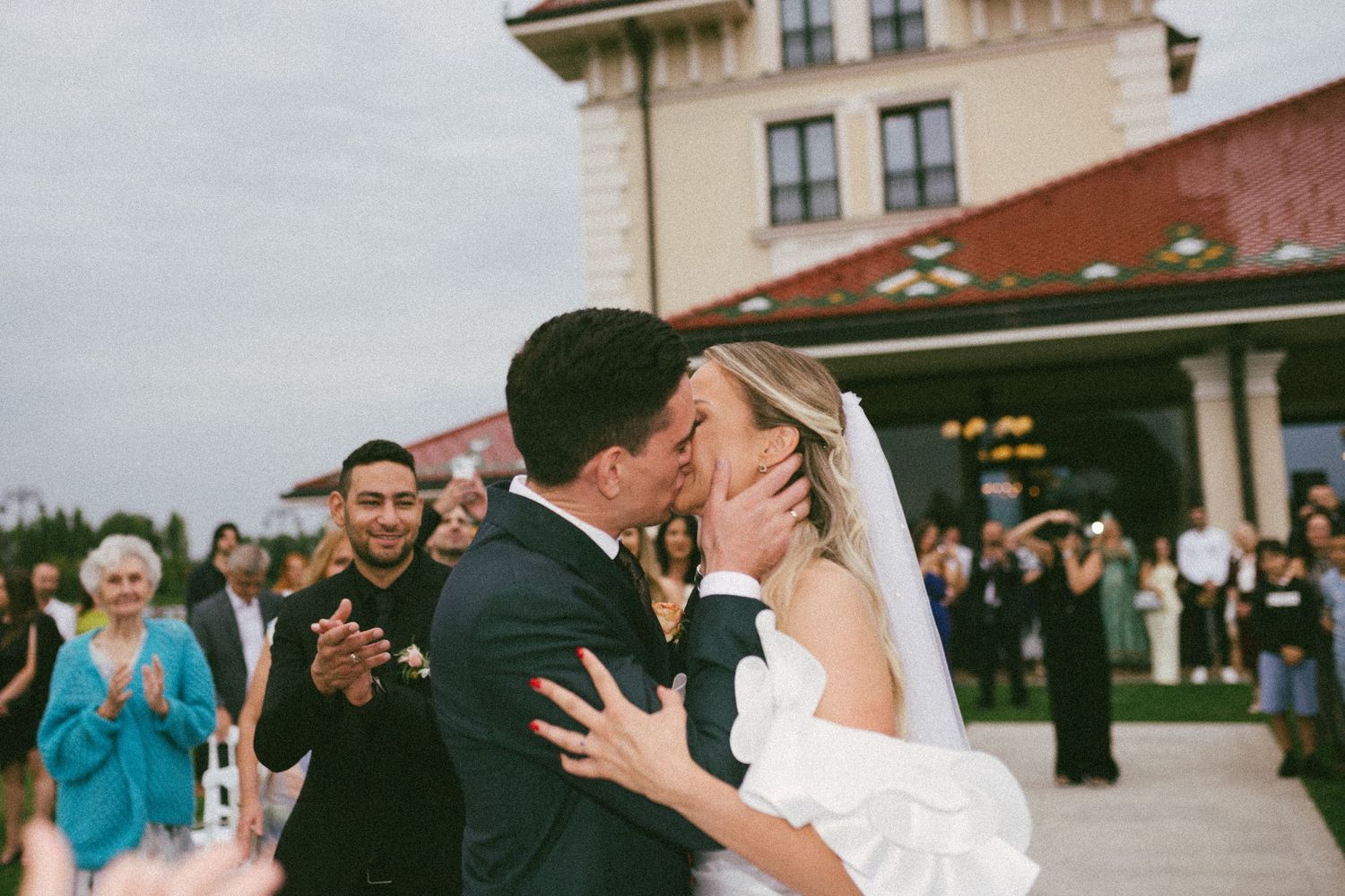 A joyful outdoor wedding celebration with guests dancing and embracing during a summer reception.