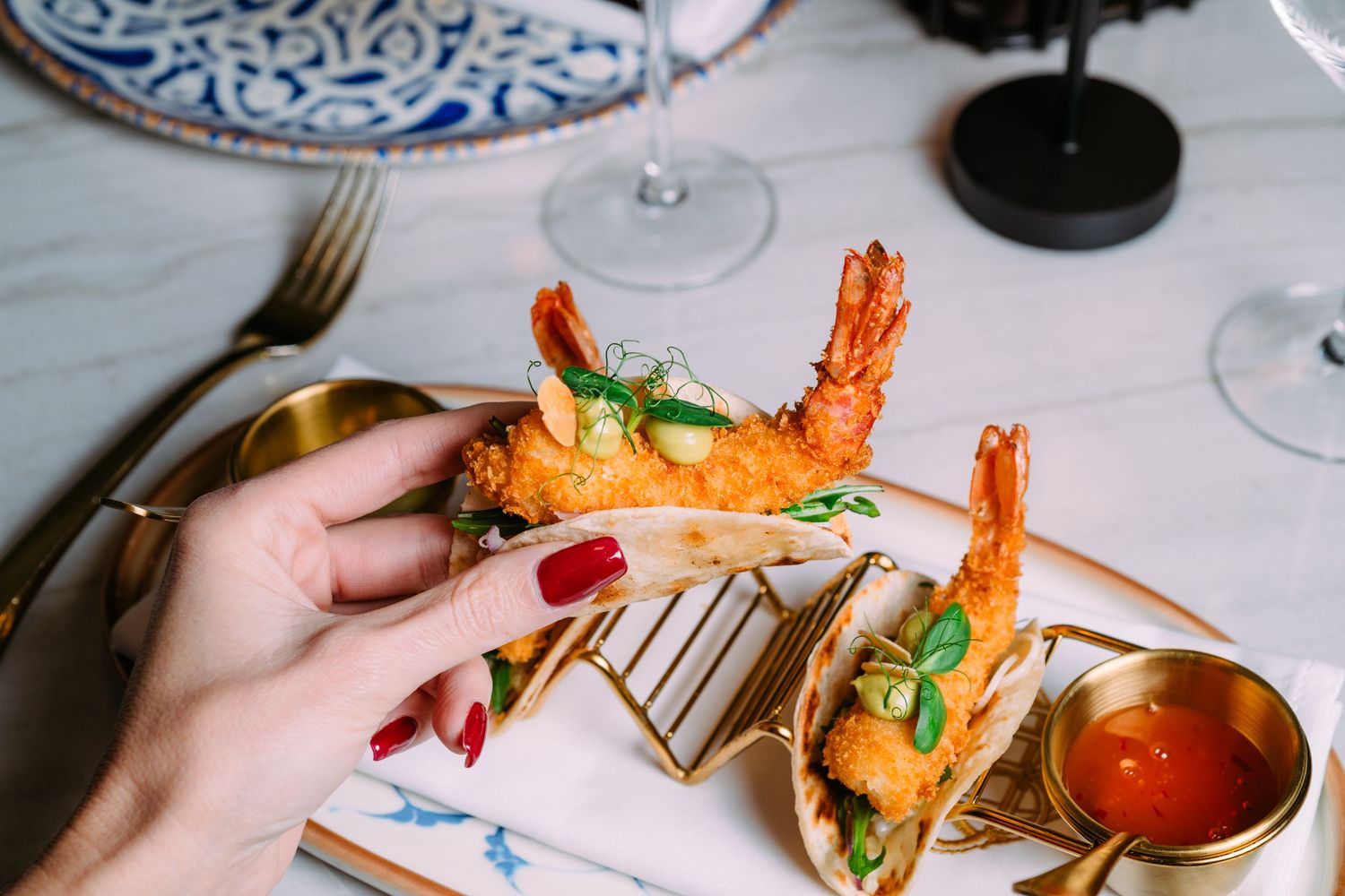 A hand serves elegant seafood dishes with prawns and garnishes on white plates at an upscale restaurant setting.