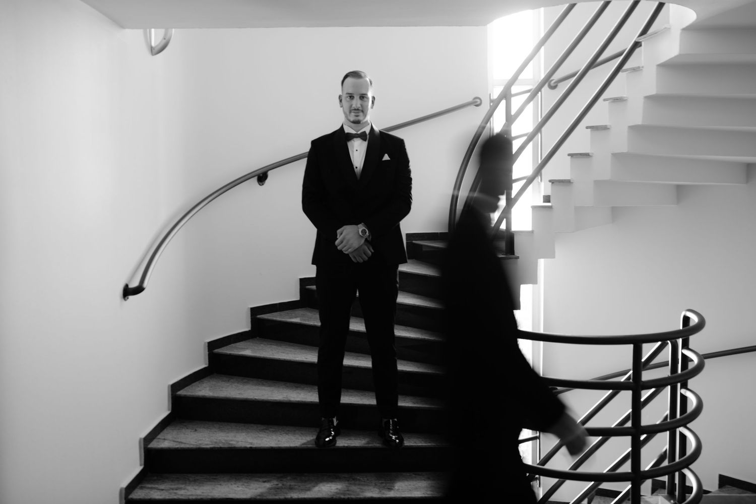 A black and white photo series showing a person descending an elegant spiral staircase in formal attire.