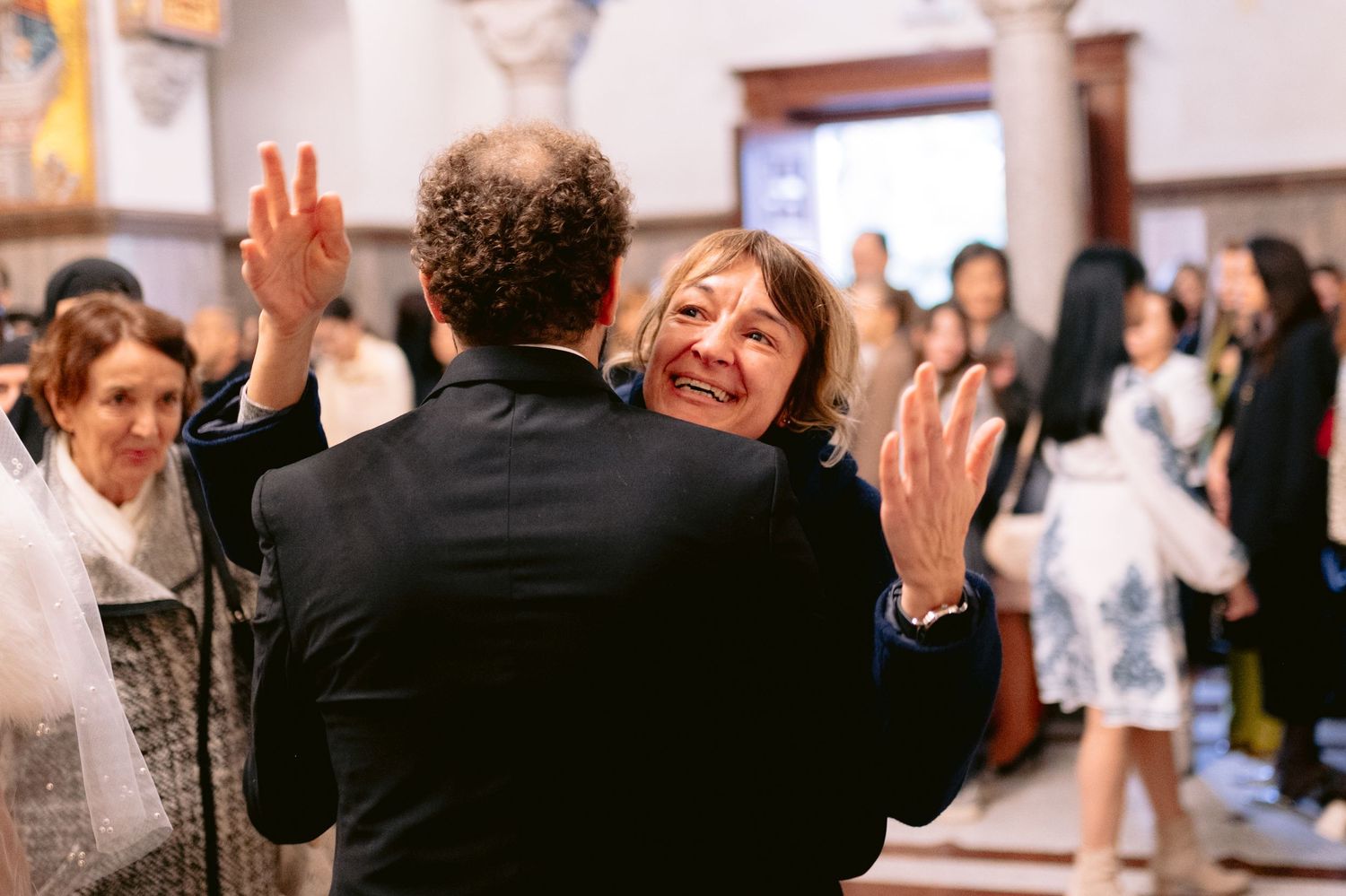 Joyful celebration captured as guests embrace during indoor wedding reception.