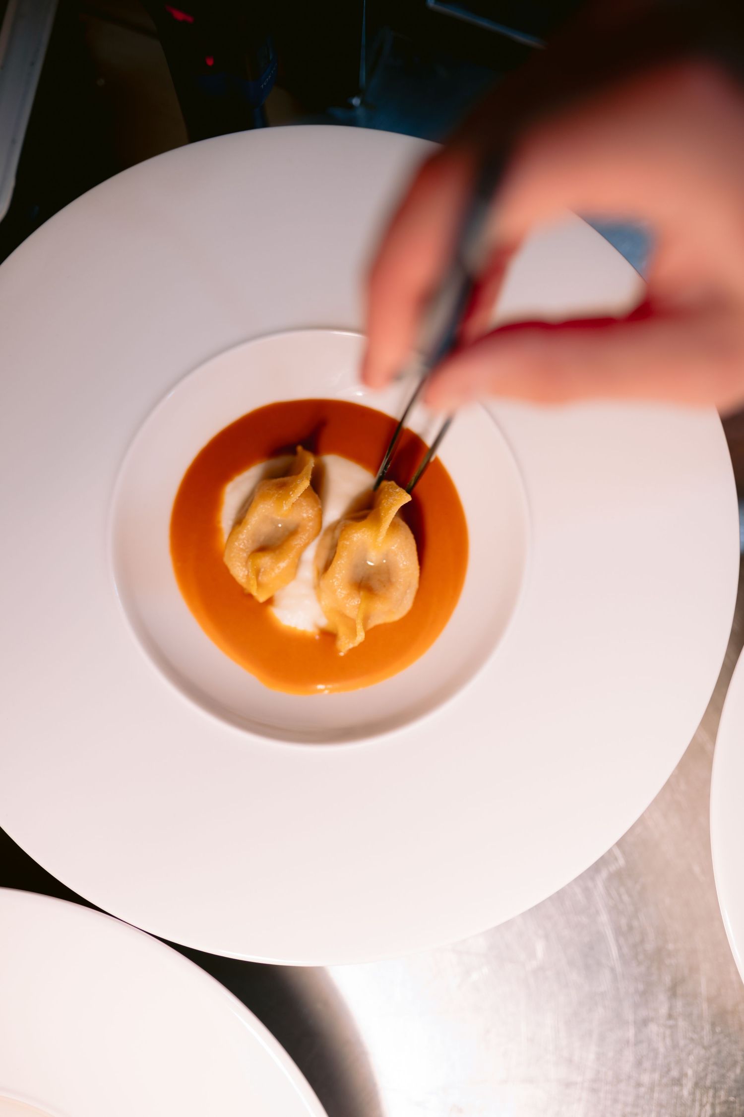 A sequence of images showing shrimp dumplings being placed in a vibrant orange tomato bisque soup on a white plate.