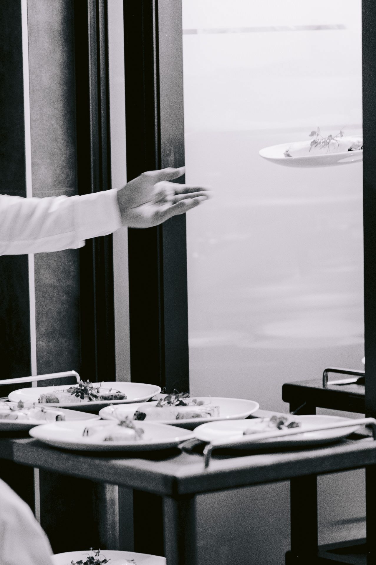 Multiple white plates arranged on dark tables in a restaurant setting.
