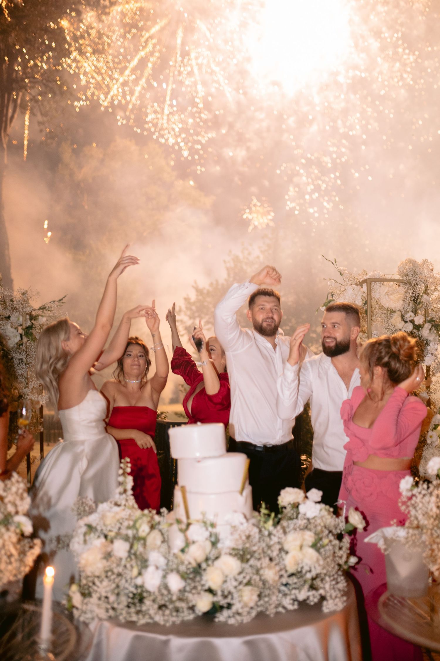 Wedding party celebrating with sparklers and cake during reception festivities.