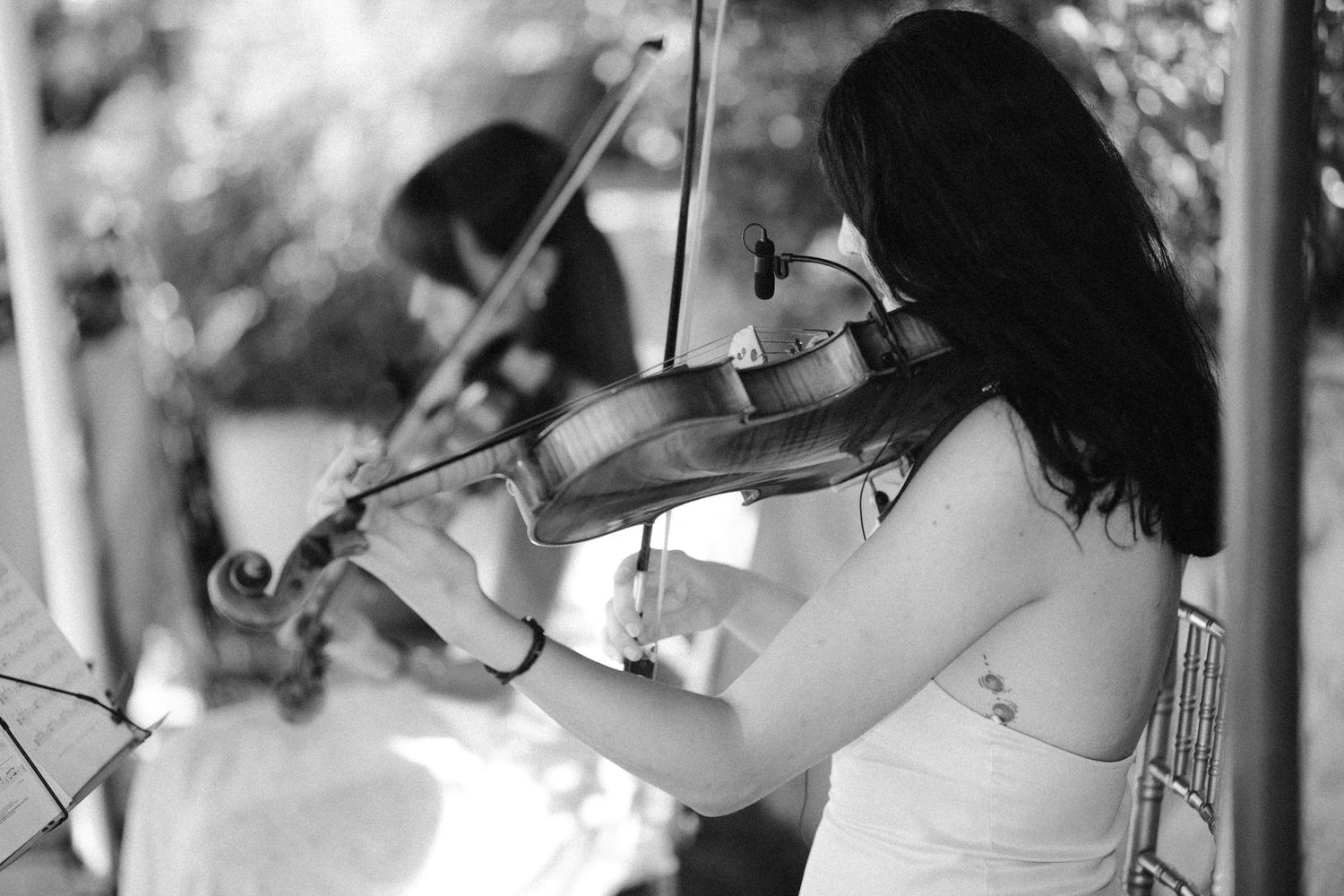 Crno-bijela fotografija dvije violinistkinje tokom nastupa na otvorenom sa fokusom na muzičarku u bijeloj haljini, Villa Slatina Banja Luka