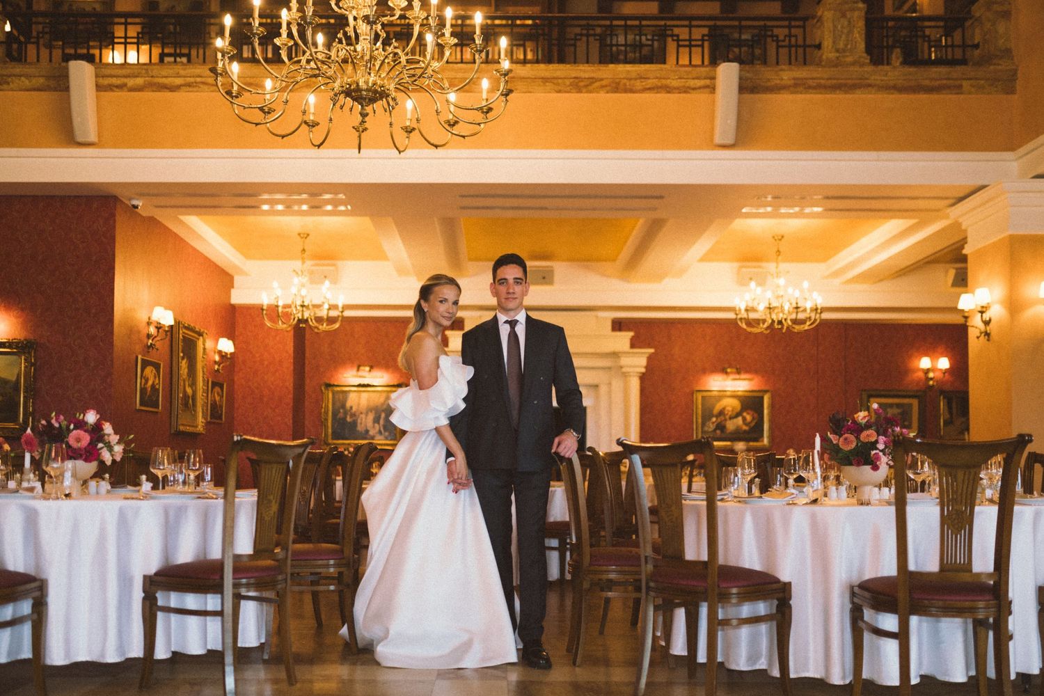 Elegant ballroom with crystal chandeliers and white tablecloths set up for a formal wedding reception.