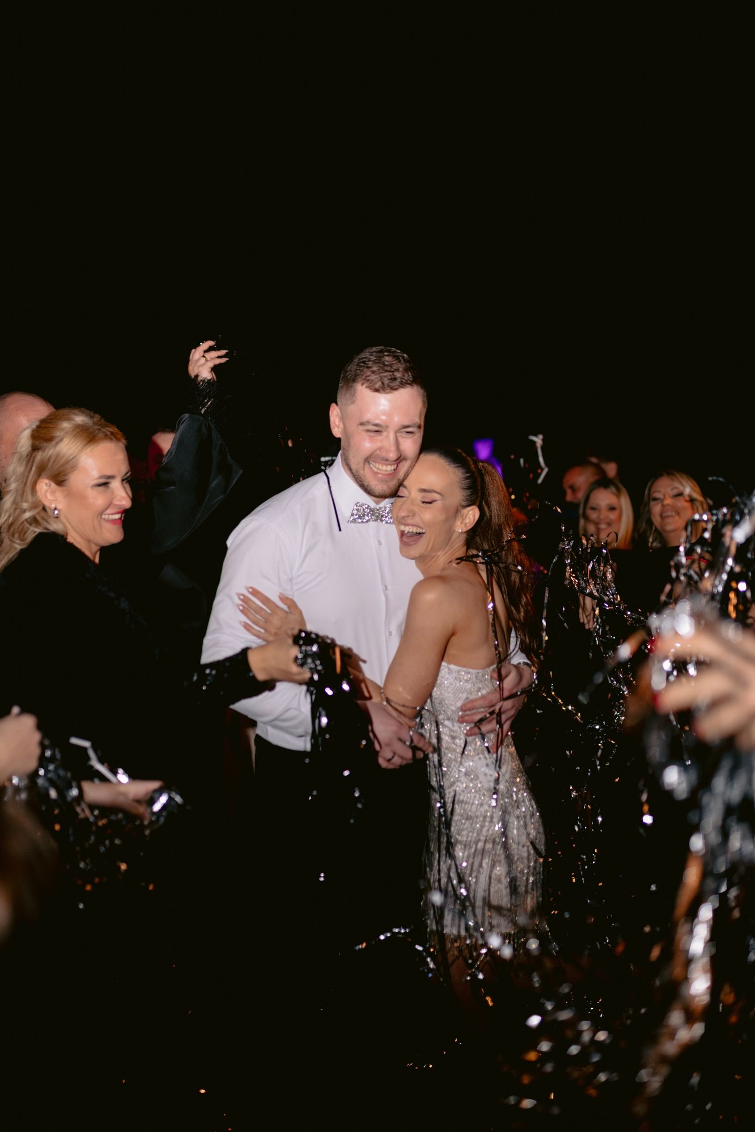 A couple in formal attire dances together while confetti falls around them at a celebration event.