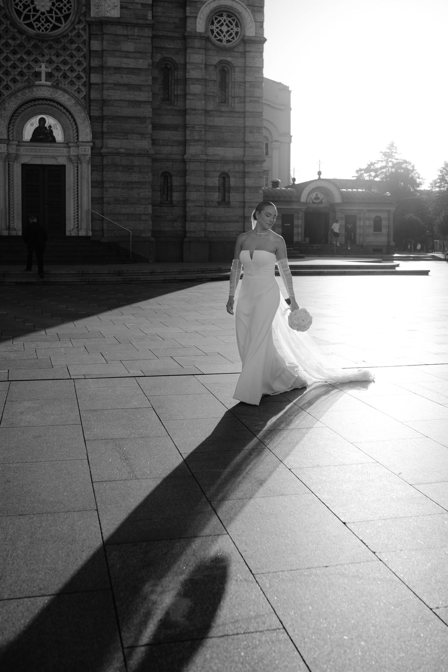 A sequence of black and white photos showing a figure in white casting long shadows on a stone plaza at sunset.