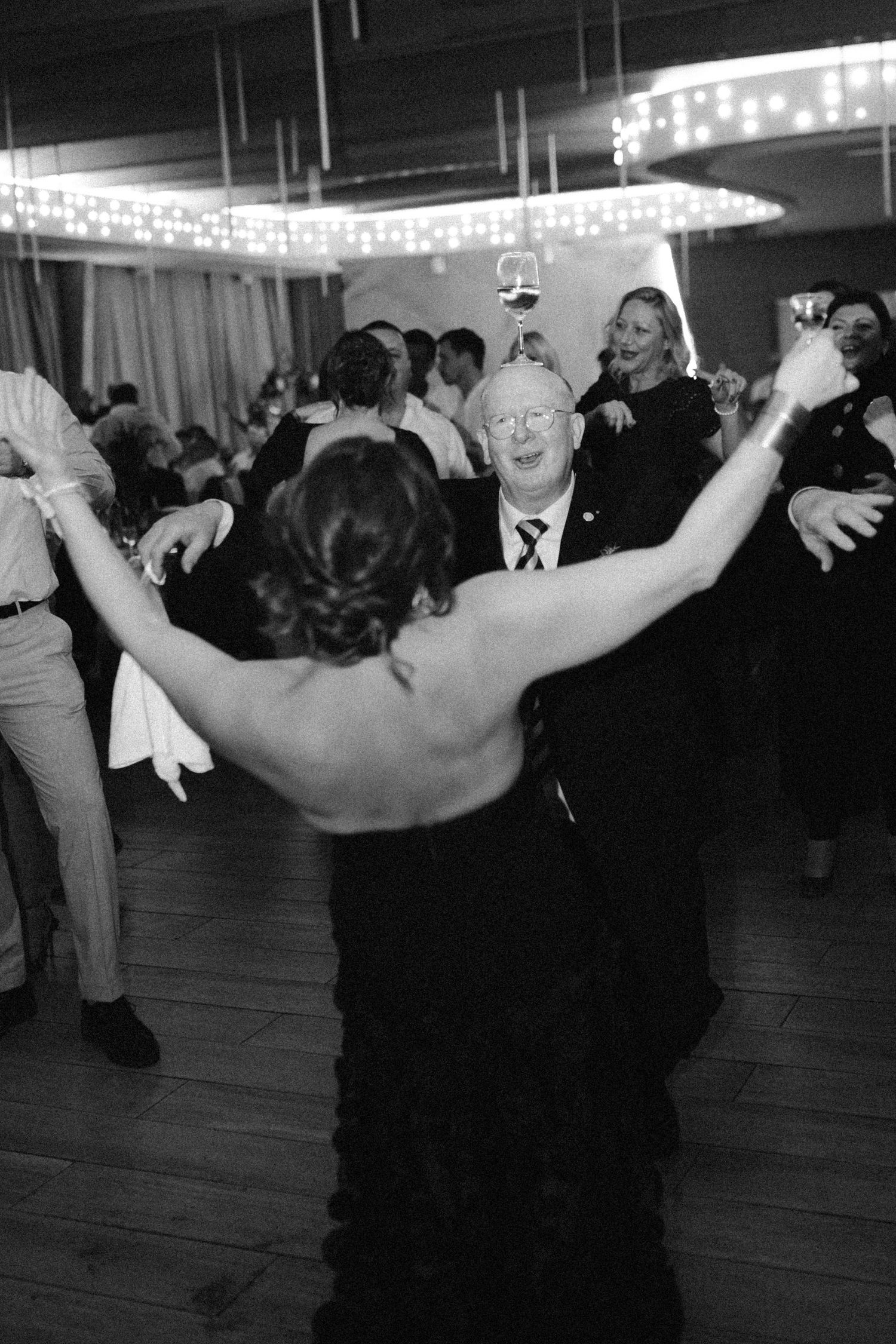 Black and white photo of wedding reception dancing with guests celebrating on dance floor.