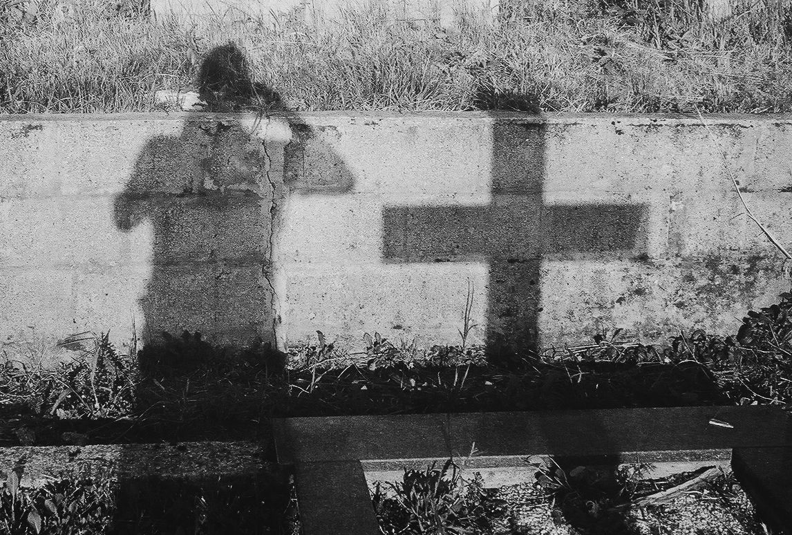 A row of silhouetted crosses and shadows cast on a white surface in black and white.