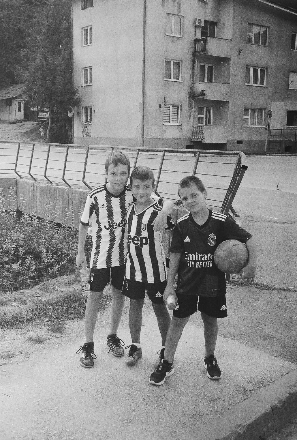 Three young soccer players in black and white striped jerseys pose together on a playground.