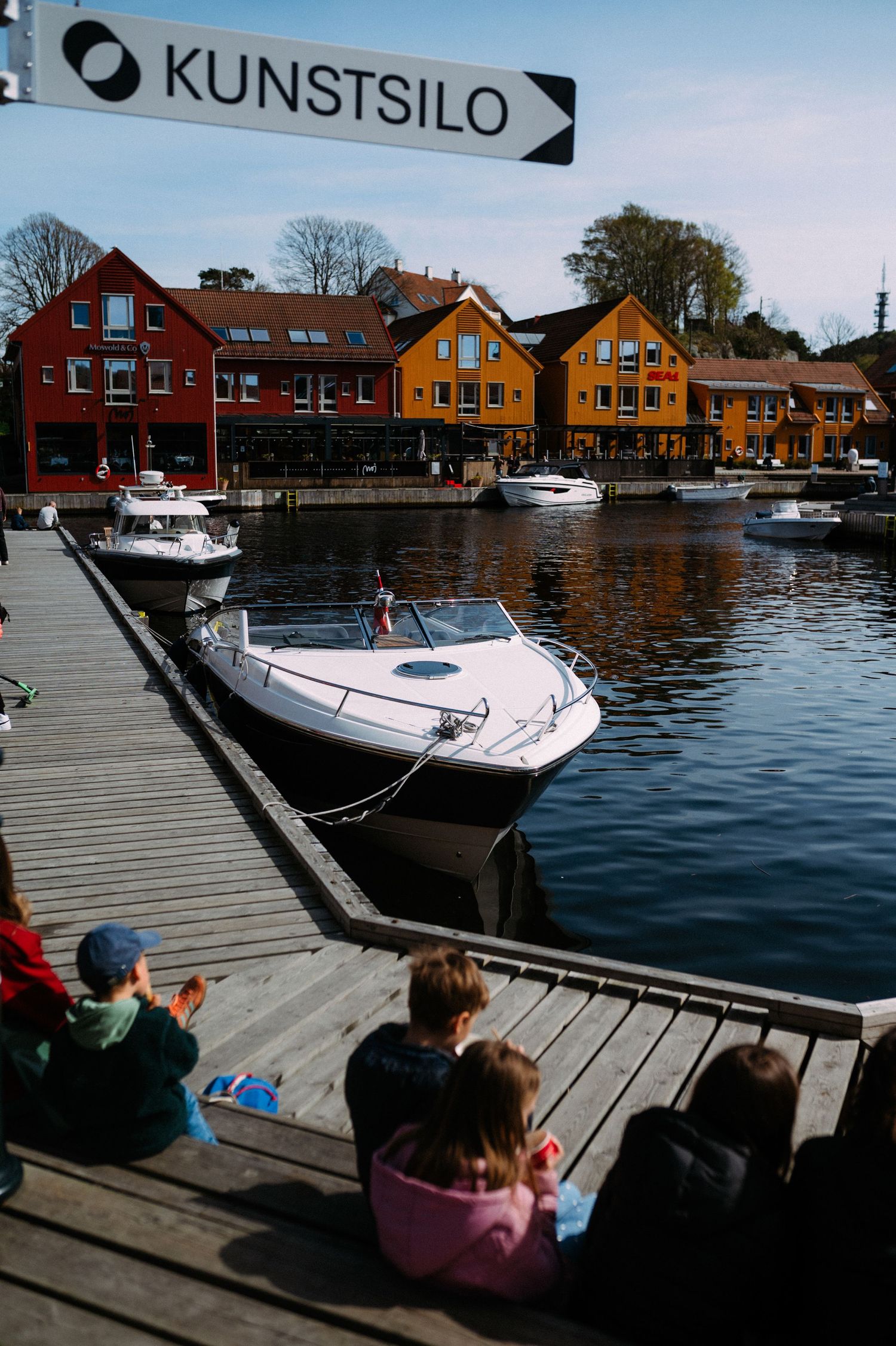 Wooden dock with boats moored alongside colorful waterfront houses in a scenic Nordic harbor.