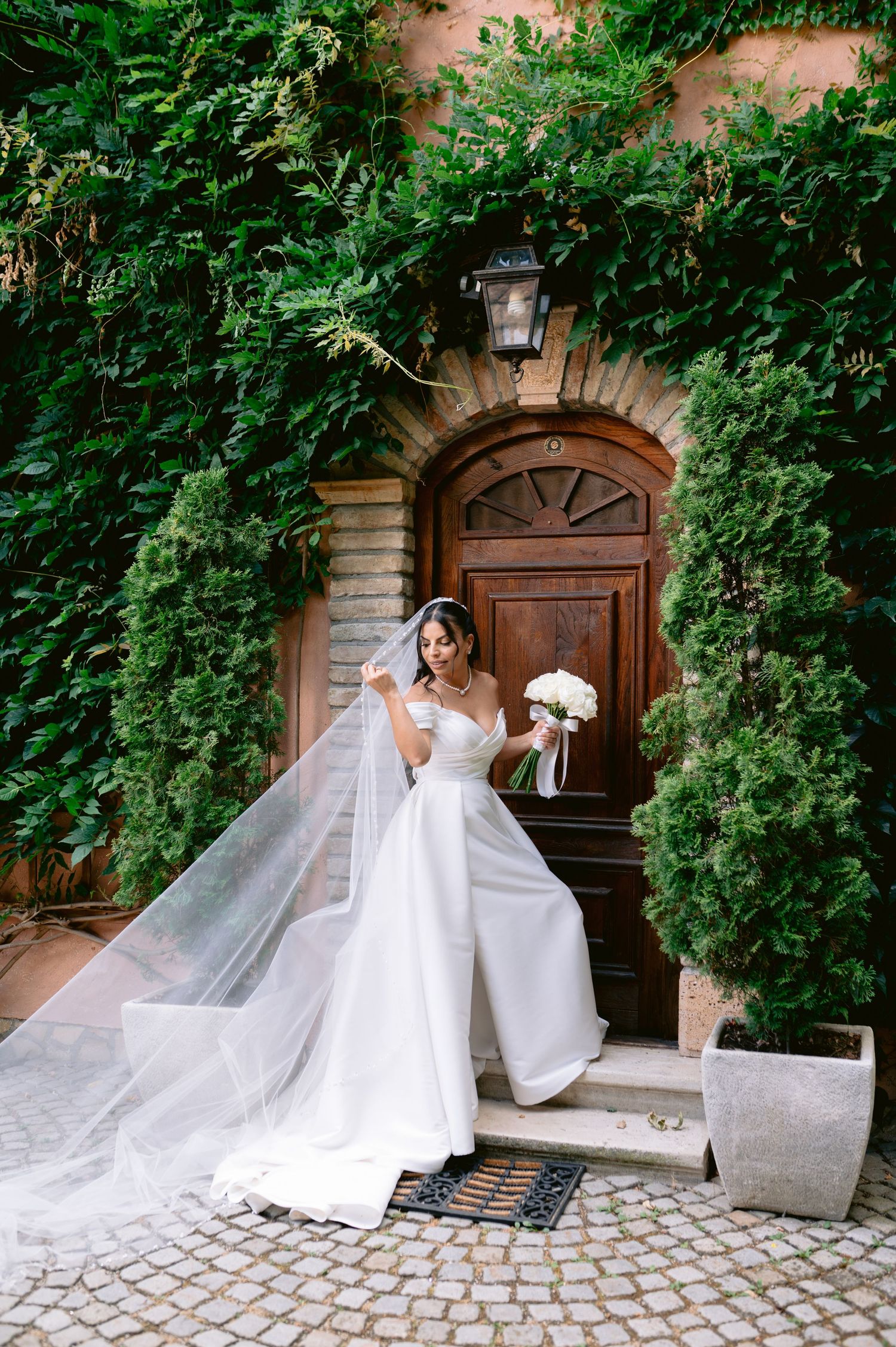 Wedding dress displayed against ivy-covered stone wall with wooden doors.