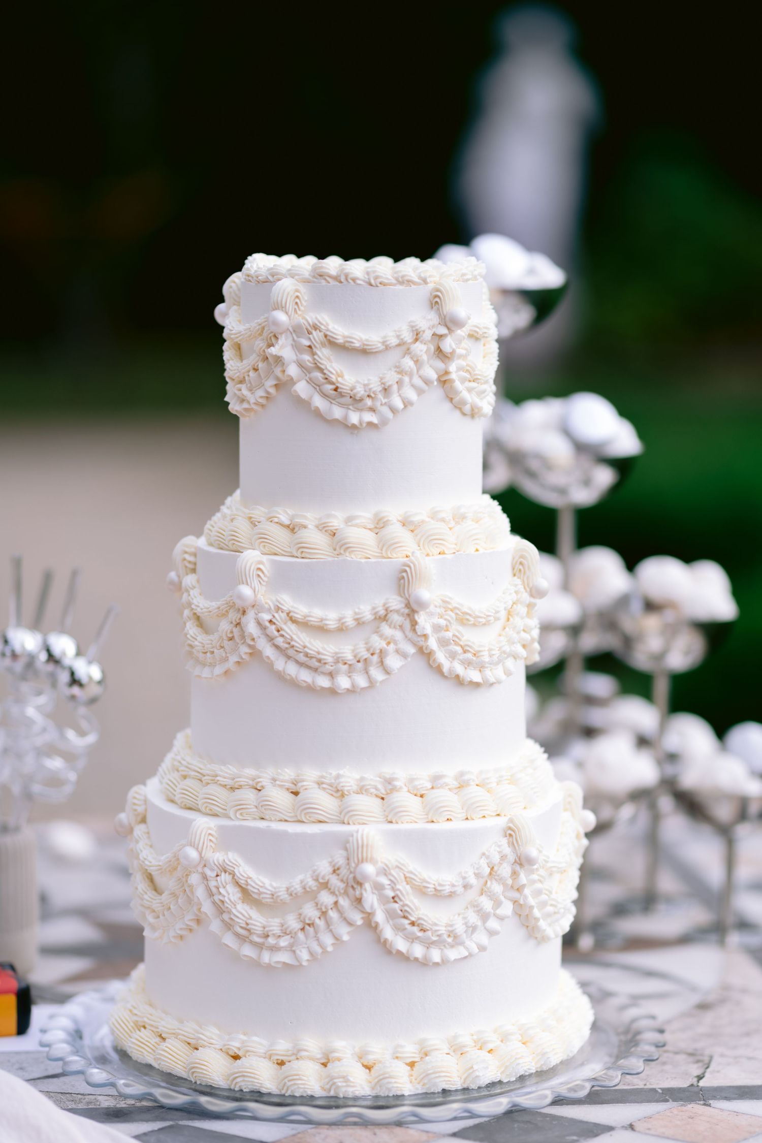 Elegant white wedding cake decorated with delicate pearl-like piping and swag details on multiple tiers.