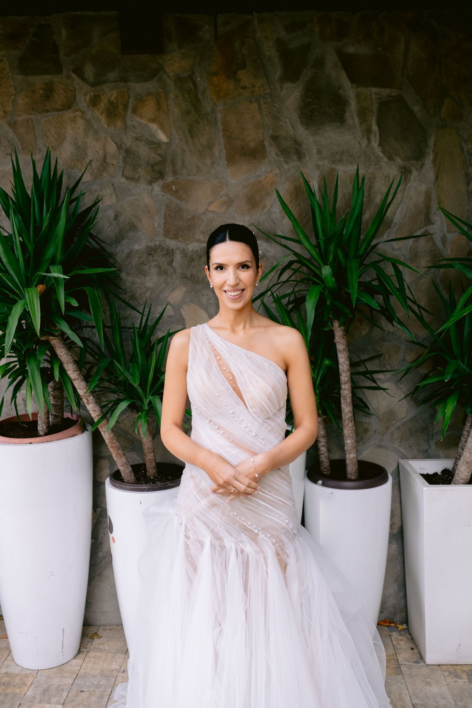 White wedding dress contrasts beautifully against stone wall with potted plants.