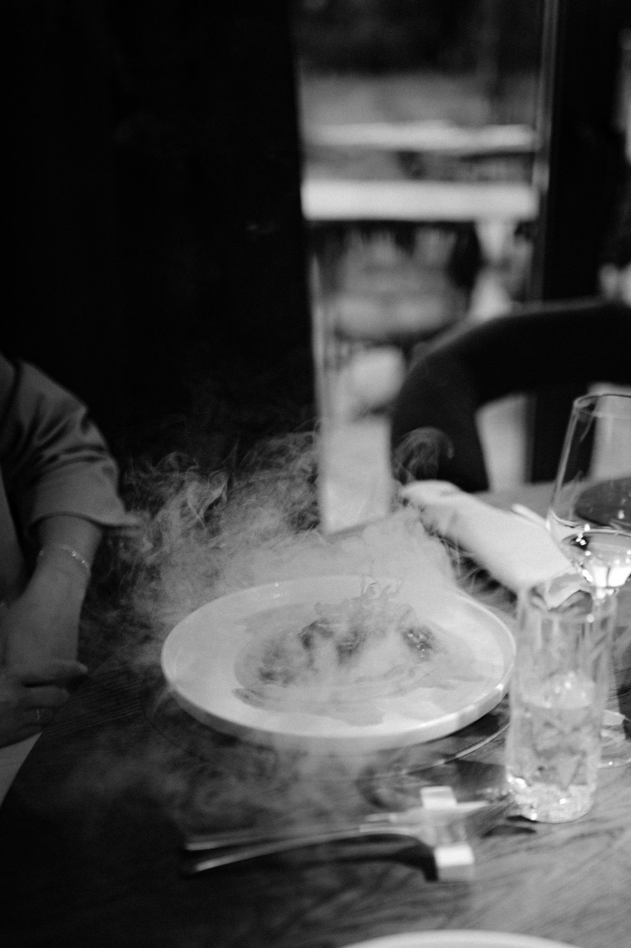 Dramatic smoke rises from plated dishes in a dark restaurant setting.