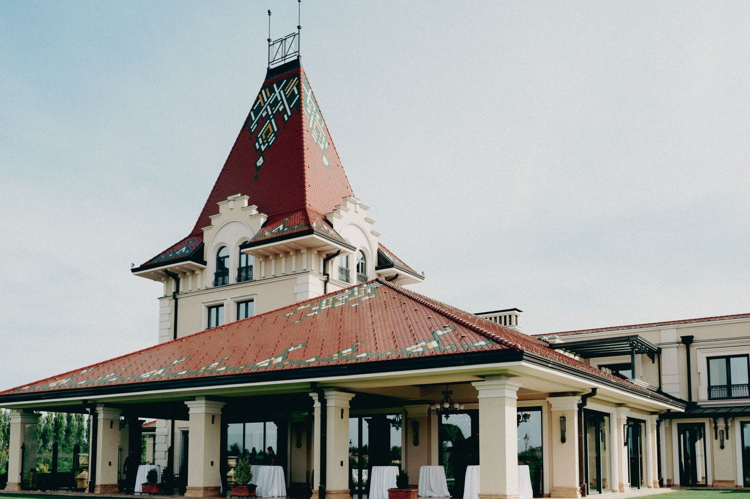 Historic train station building with distinctive red roof and ornate tower stands against light blue sky.