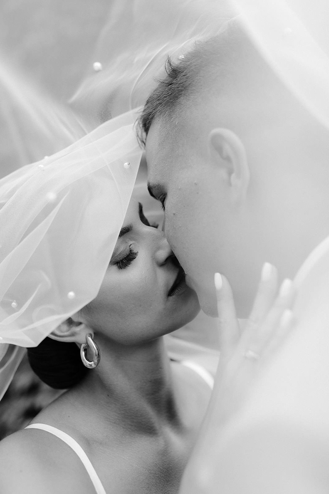 Intimate black and white close-up of a couple kissing under a delicate veil.