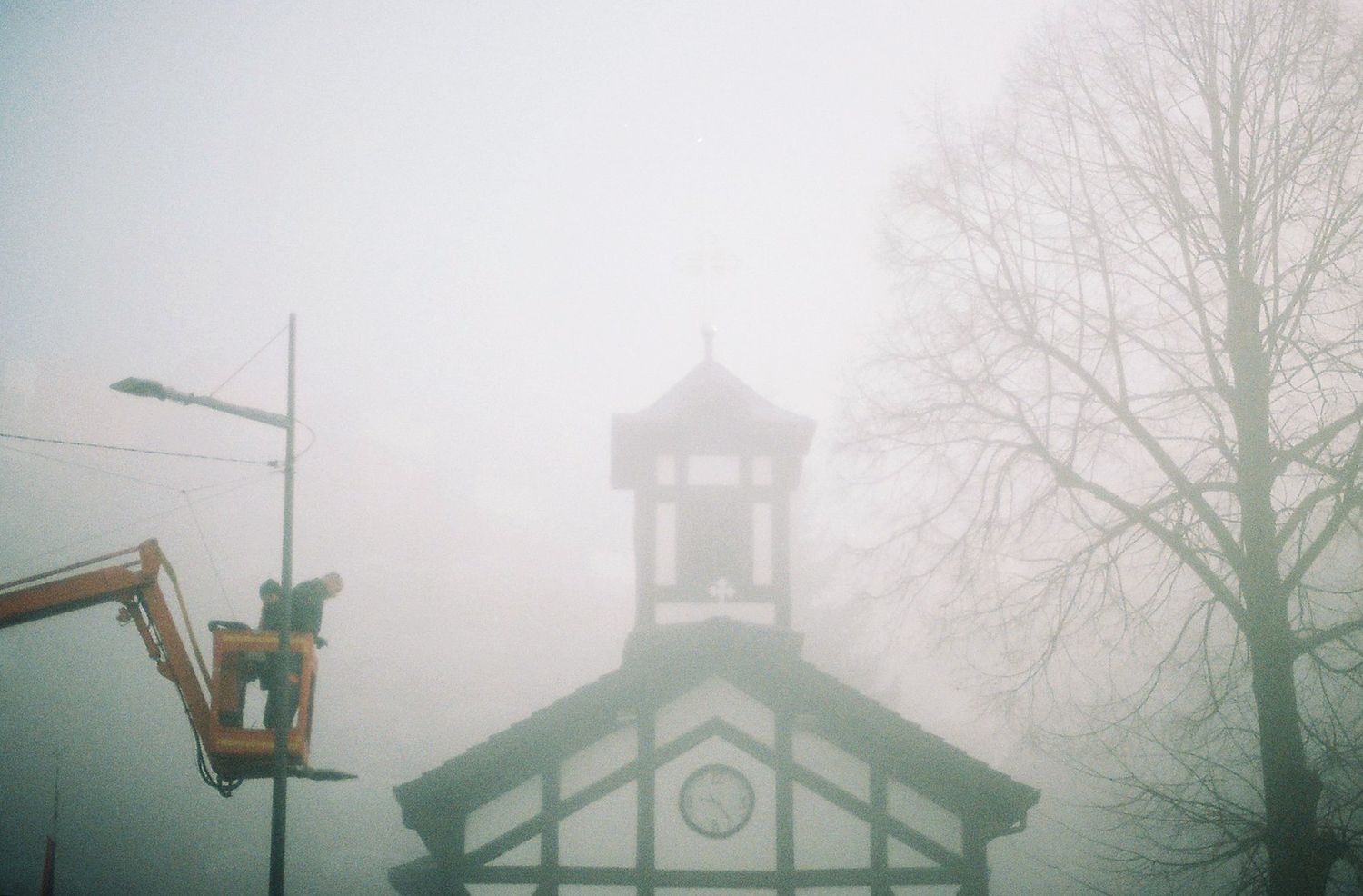Foggy morning view of a church steeple and bare trees creating a moody, atmospheric scene.