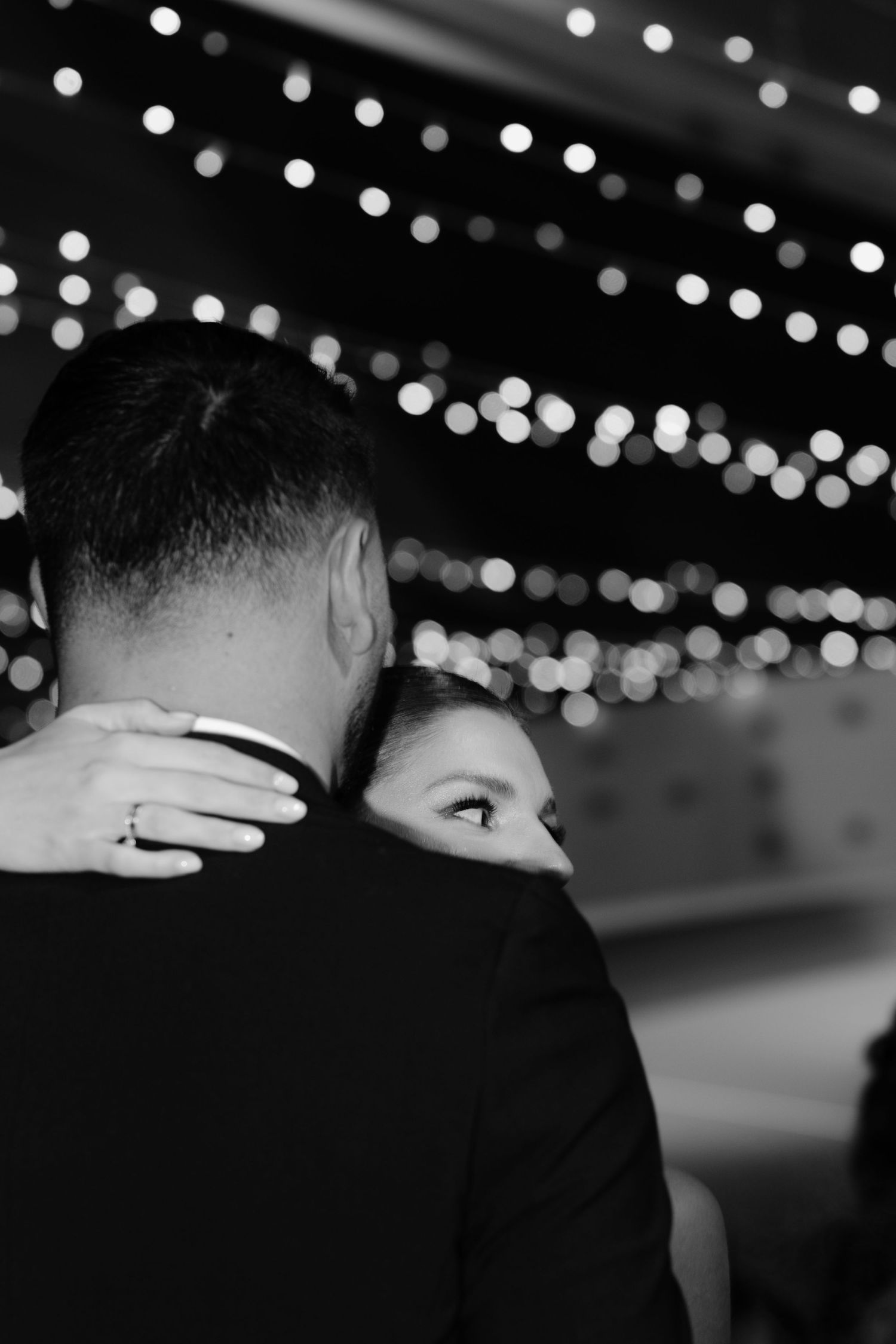 Black and white photo of string lights hanging overhead creating a romantic ambiance at an evening event.